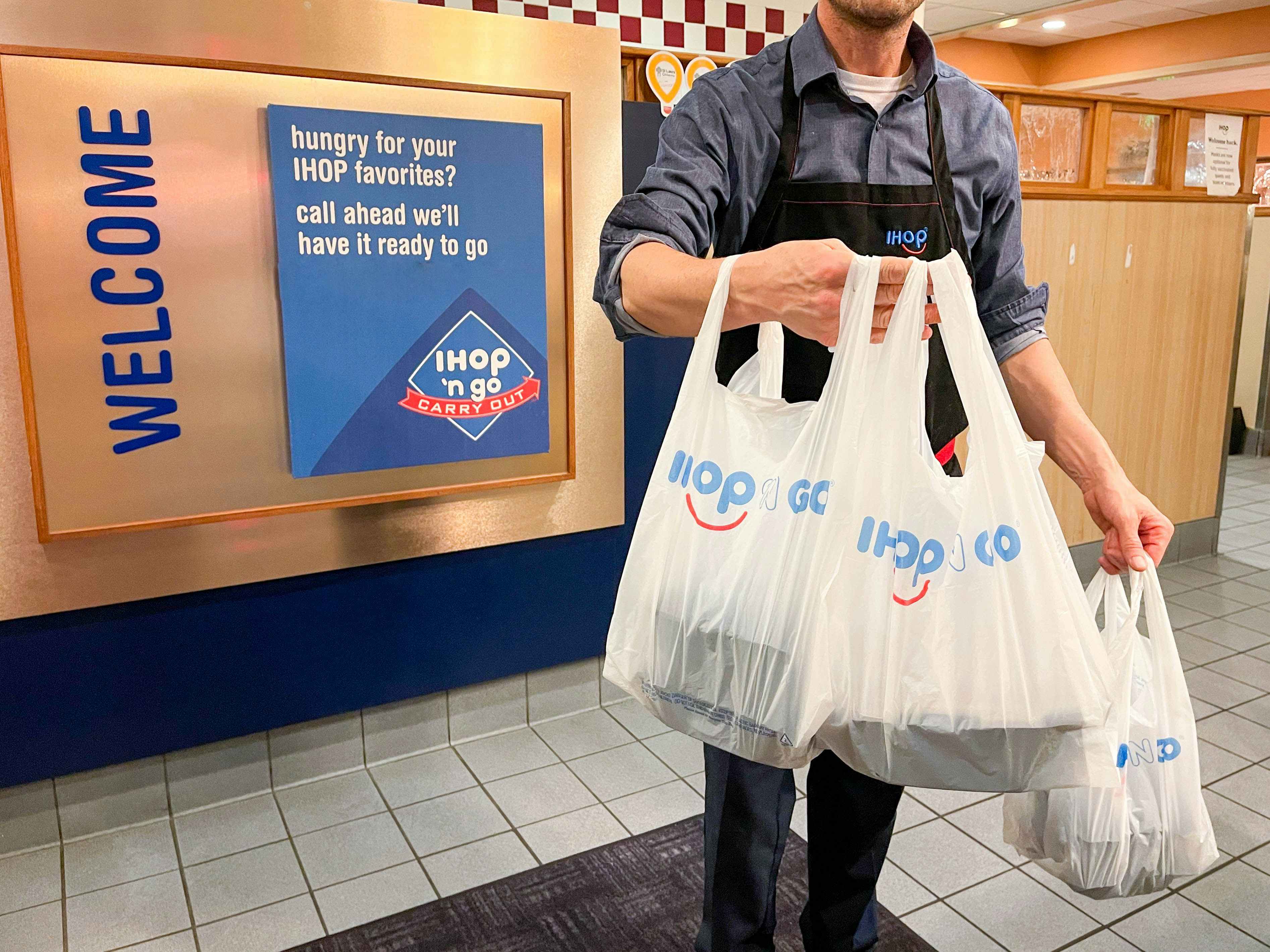 An IHOP employee holding some bags of IHOP to go orders.