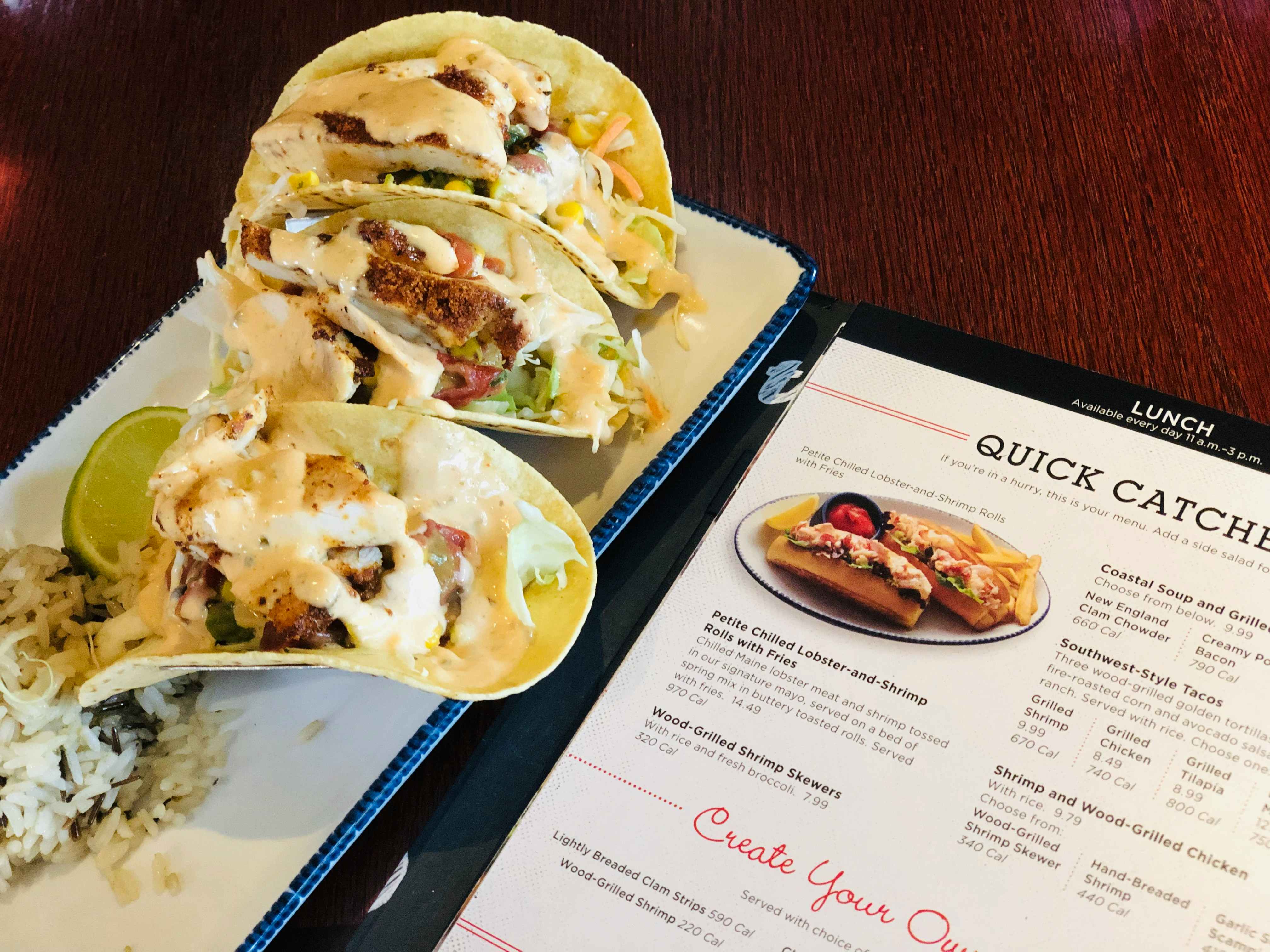 Three Red Lobster Southwest-style tacos sitting on a plate next to a menu open to the Red Lobster lunch options.