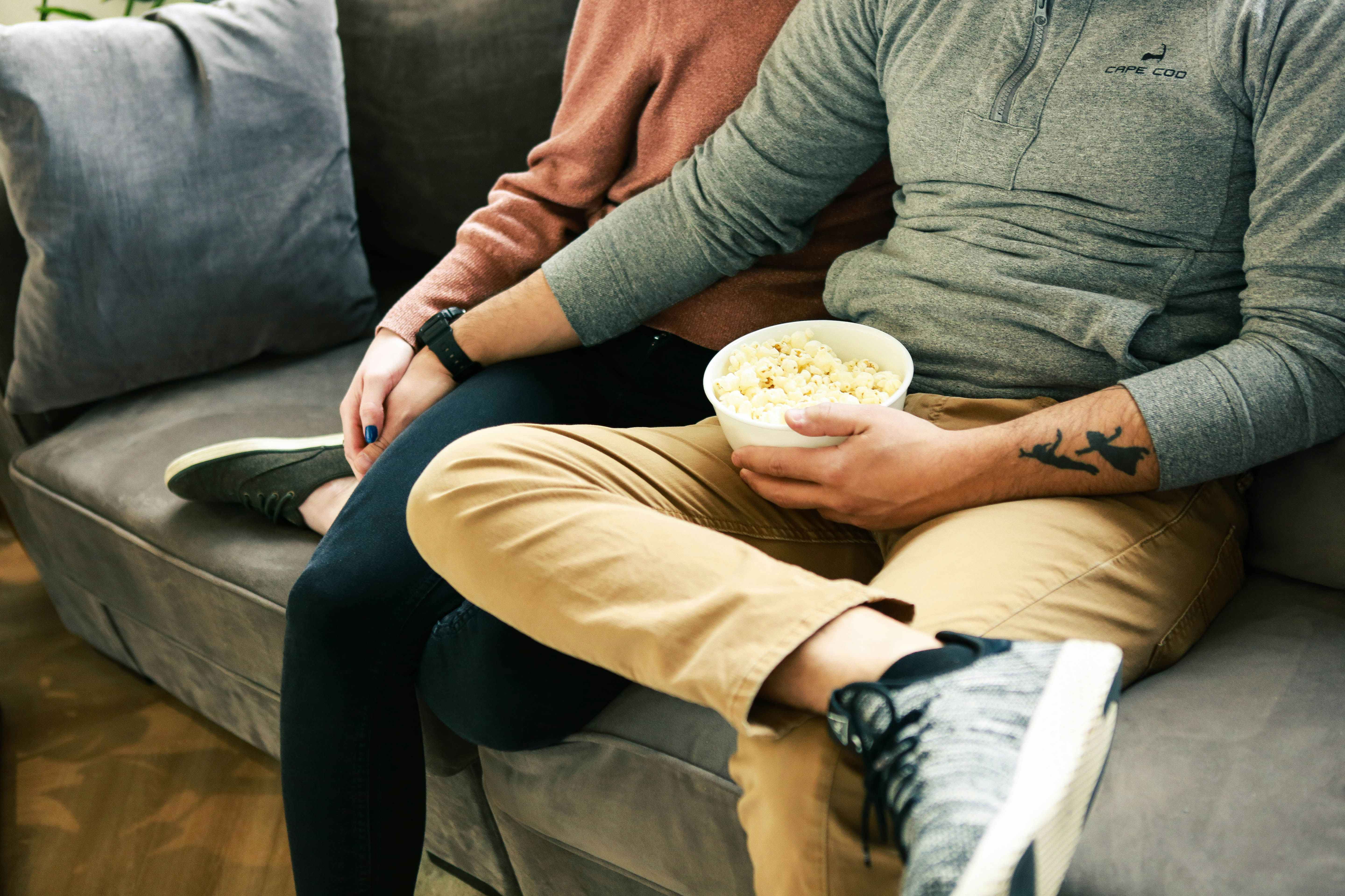 a couple holding hands eating popcorn on the couch 