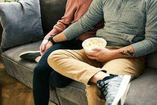 a couple holding hands eating popcorn on the couch