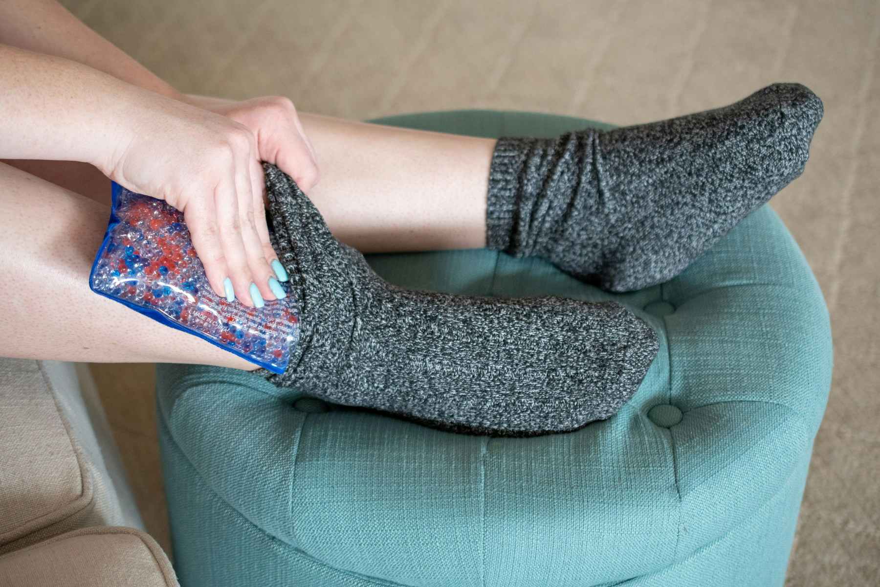 A person putting an ice gel pack under a sock on their foot.