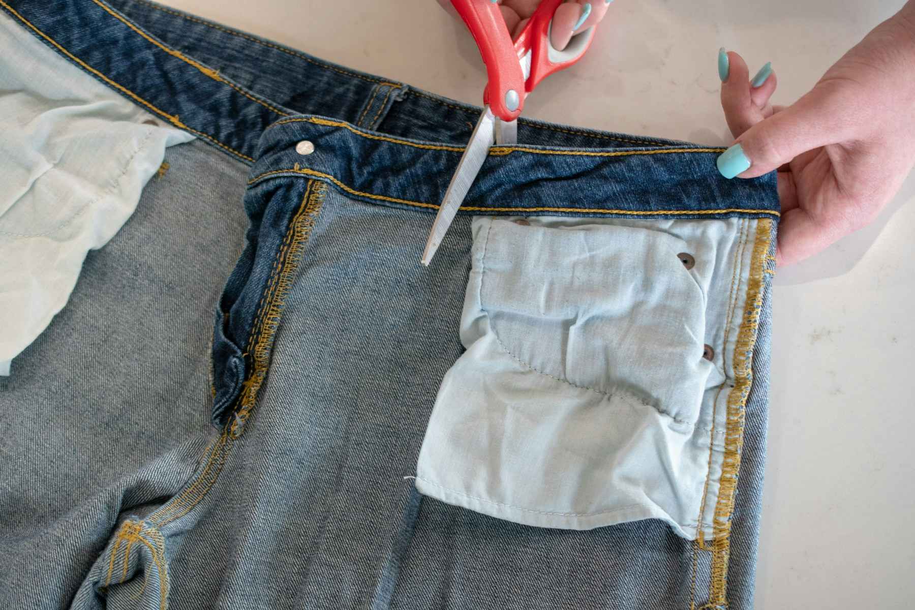 A person cutting out the pocket of a pair of jeans.