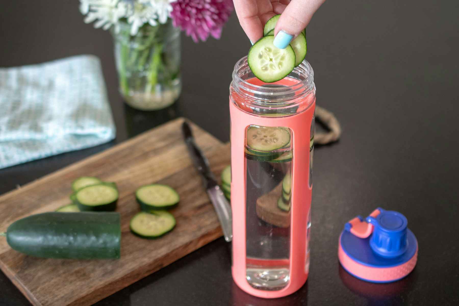 A person adding cucumber slices to a bottle of water.