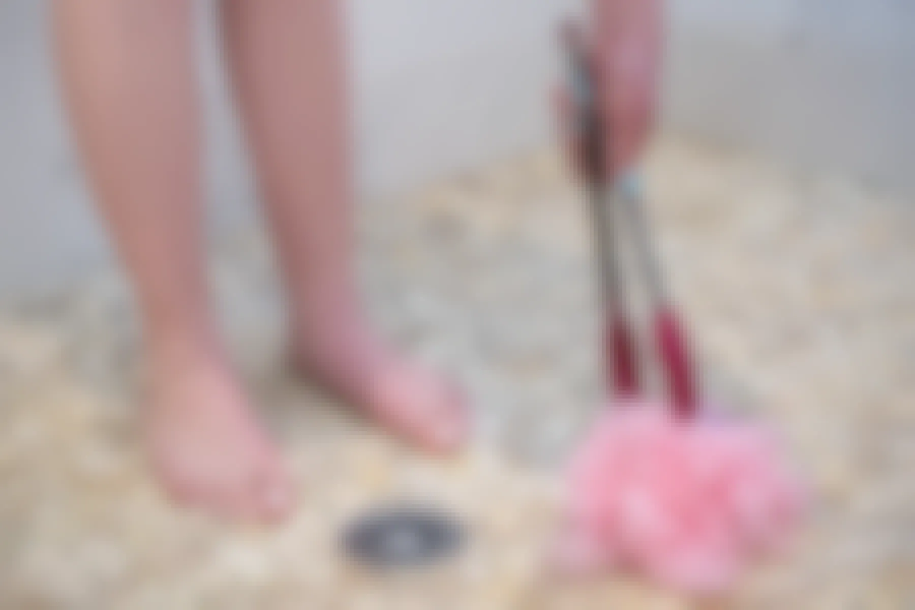 A person picking up a loofa off a shower floor using a pair of tongs.