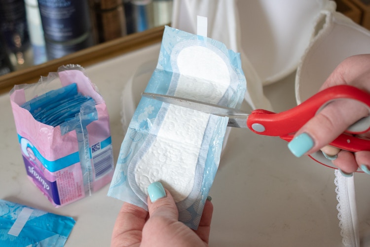 A person cutting a pantiliner in half with scissors.