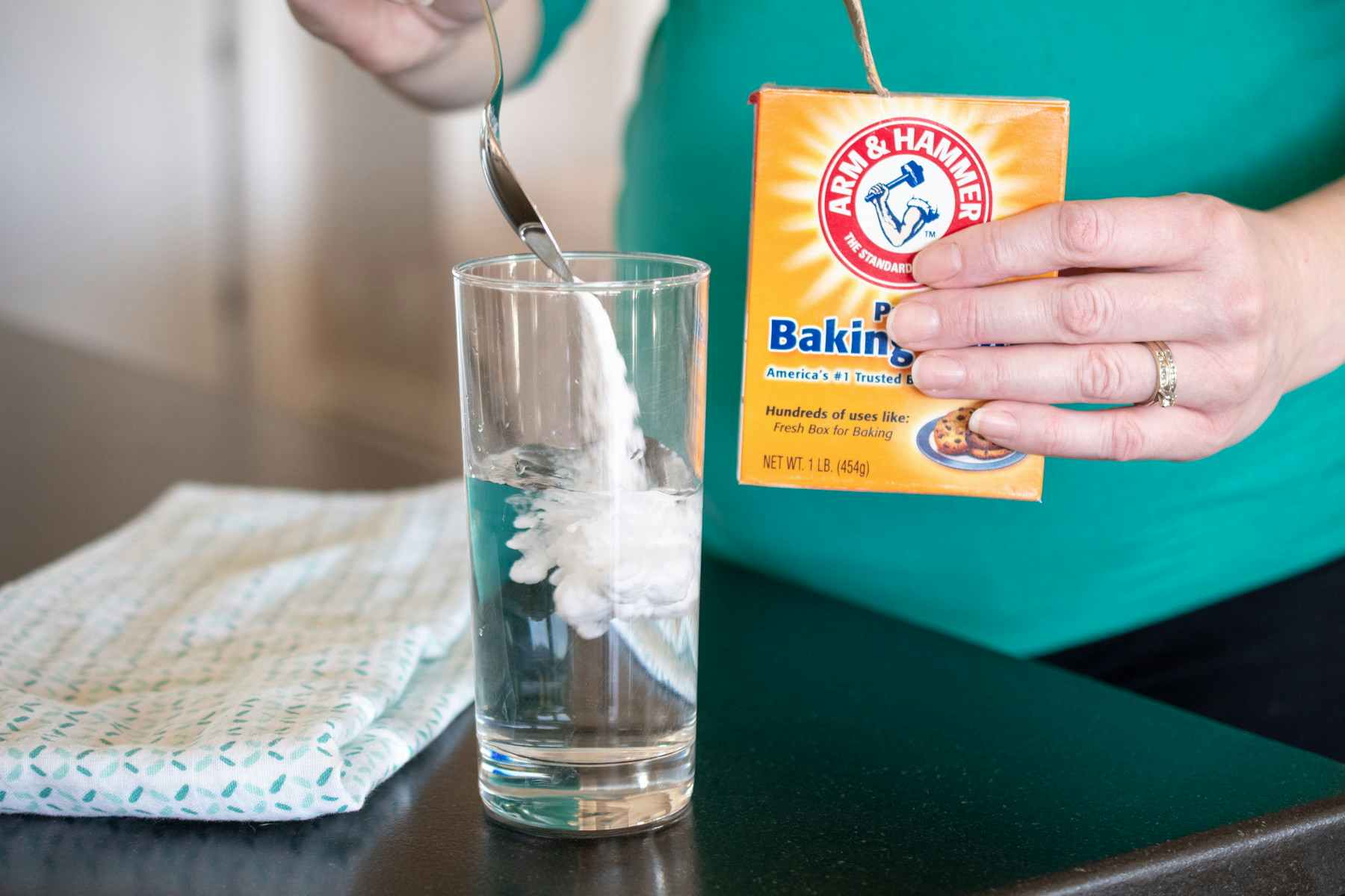 A pregnant woman putting baking soda into a glass of water.