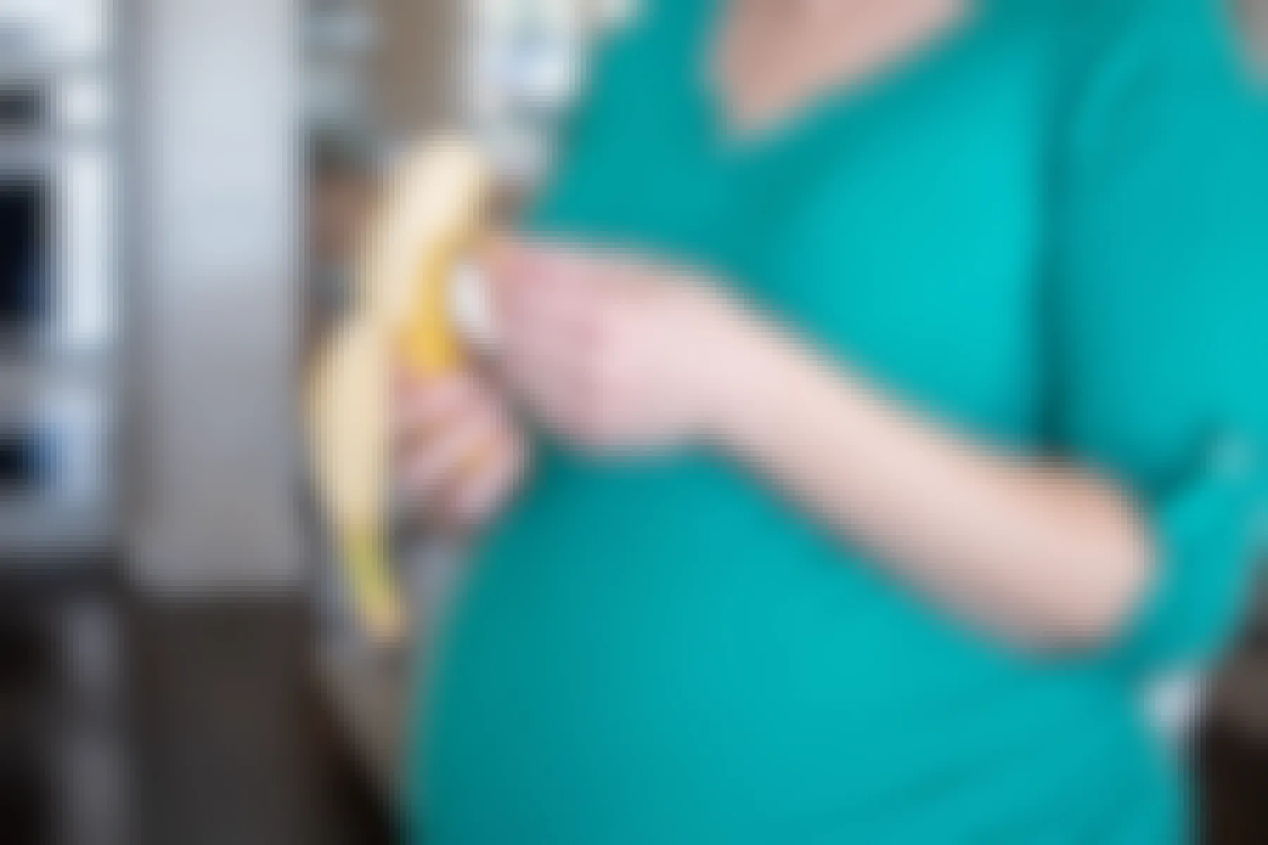 A pregnant woman peeling a banana.