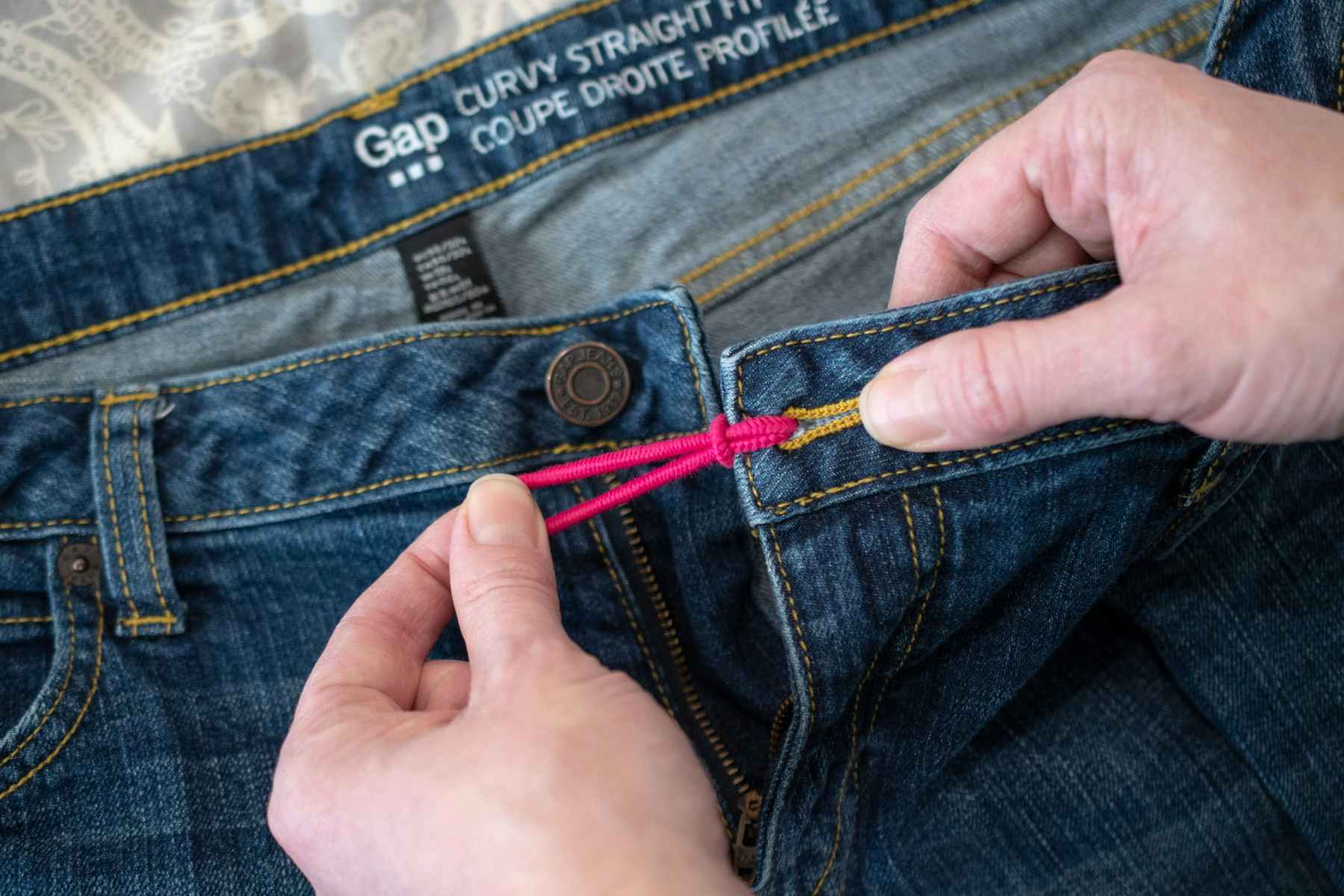A person putting a hair tie in the button hole of a pair of jeans.