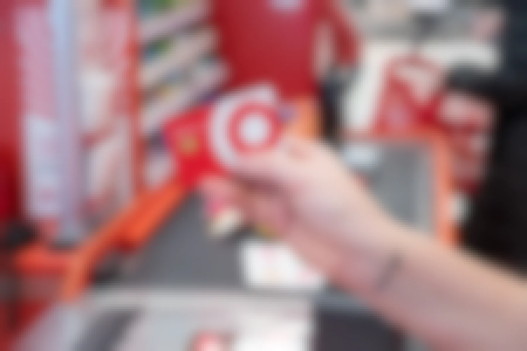 A person's hand holding a Target RedCard up in front of the checkout lane at Target.