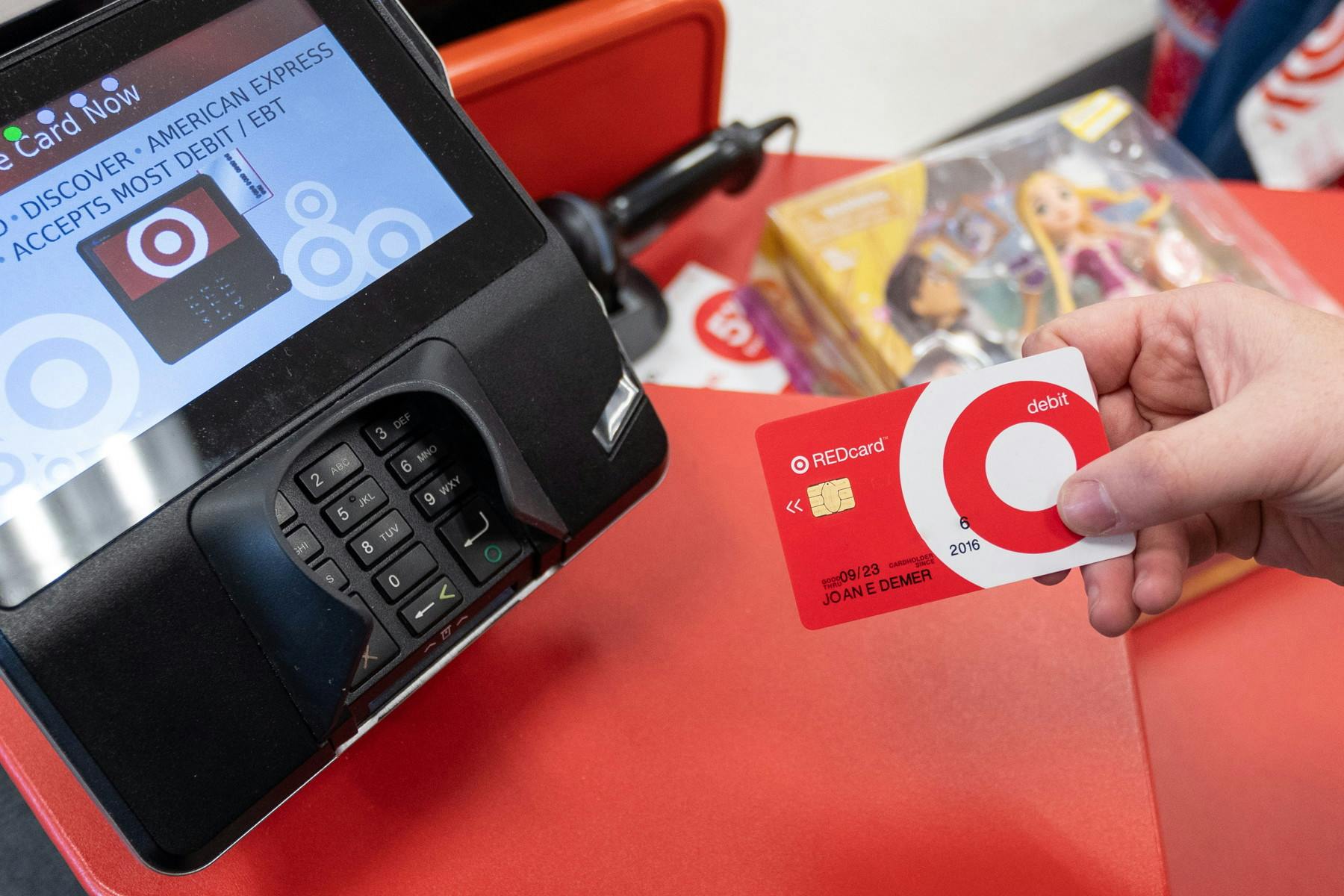 A person's hand holding their Target RedCard next to a point of sale machine at the Target checkout.