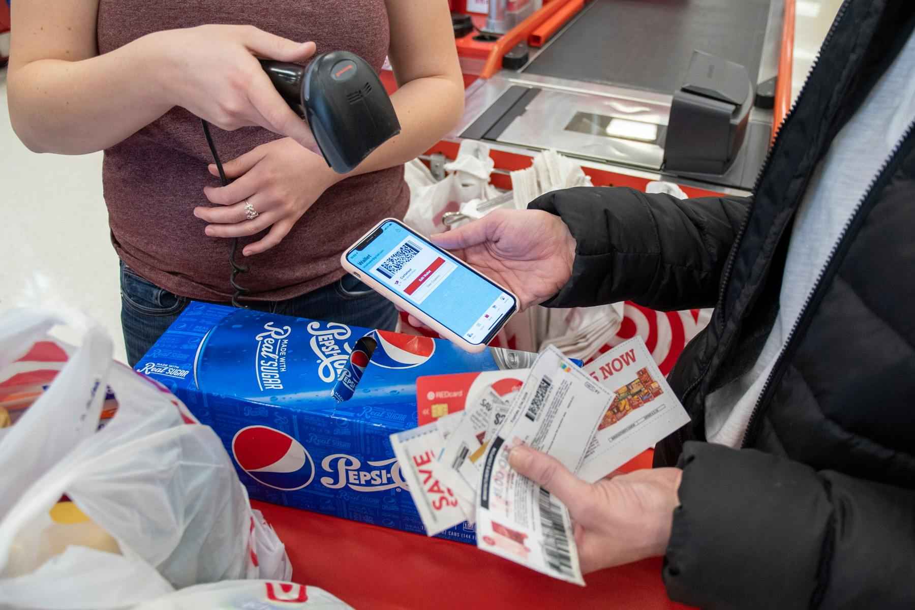 A person standing at the Target checkout, holding up their phone displaying their Target app barcode, and another person using the hand scanner to scan the phone.