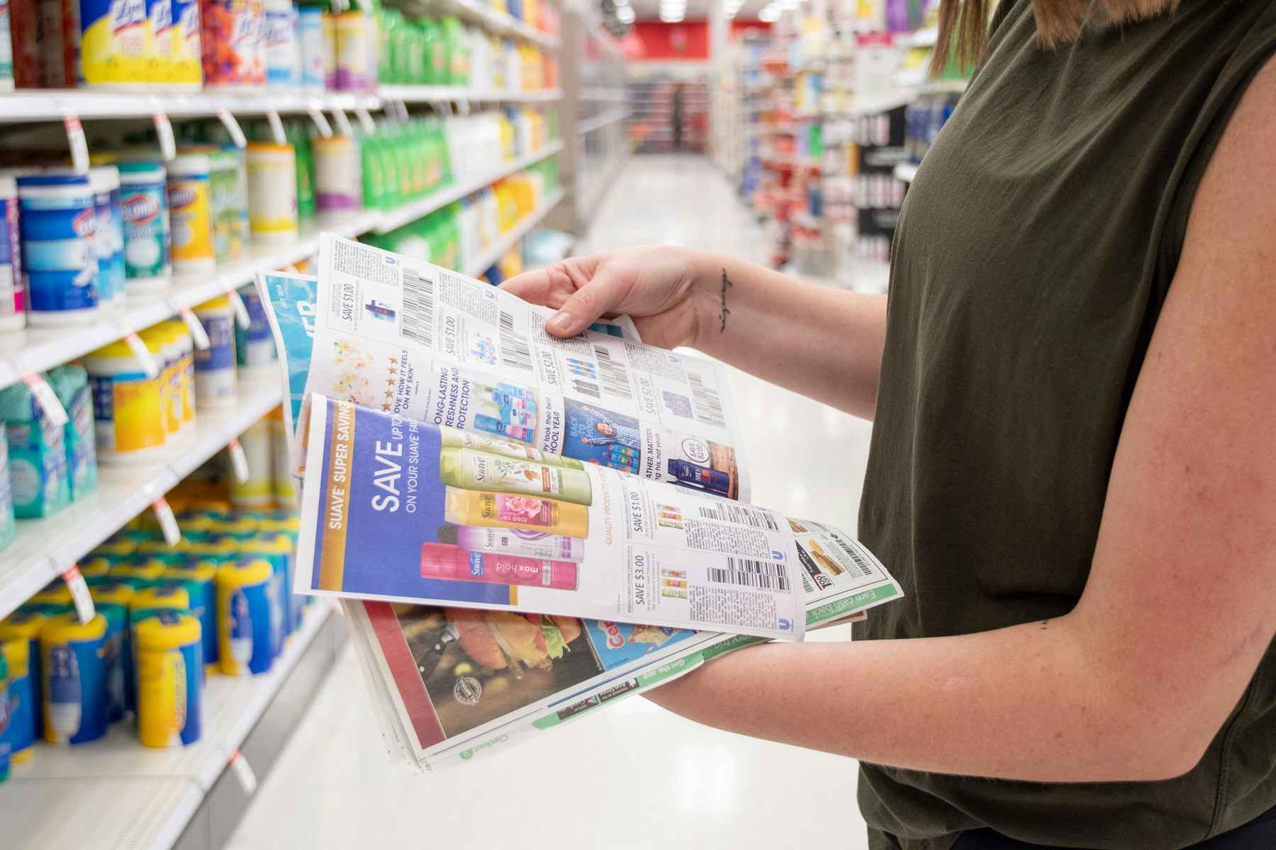 A woman flipping through newspaper coupons in a grocery store aisle 