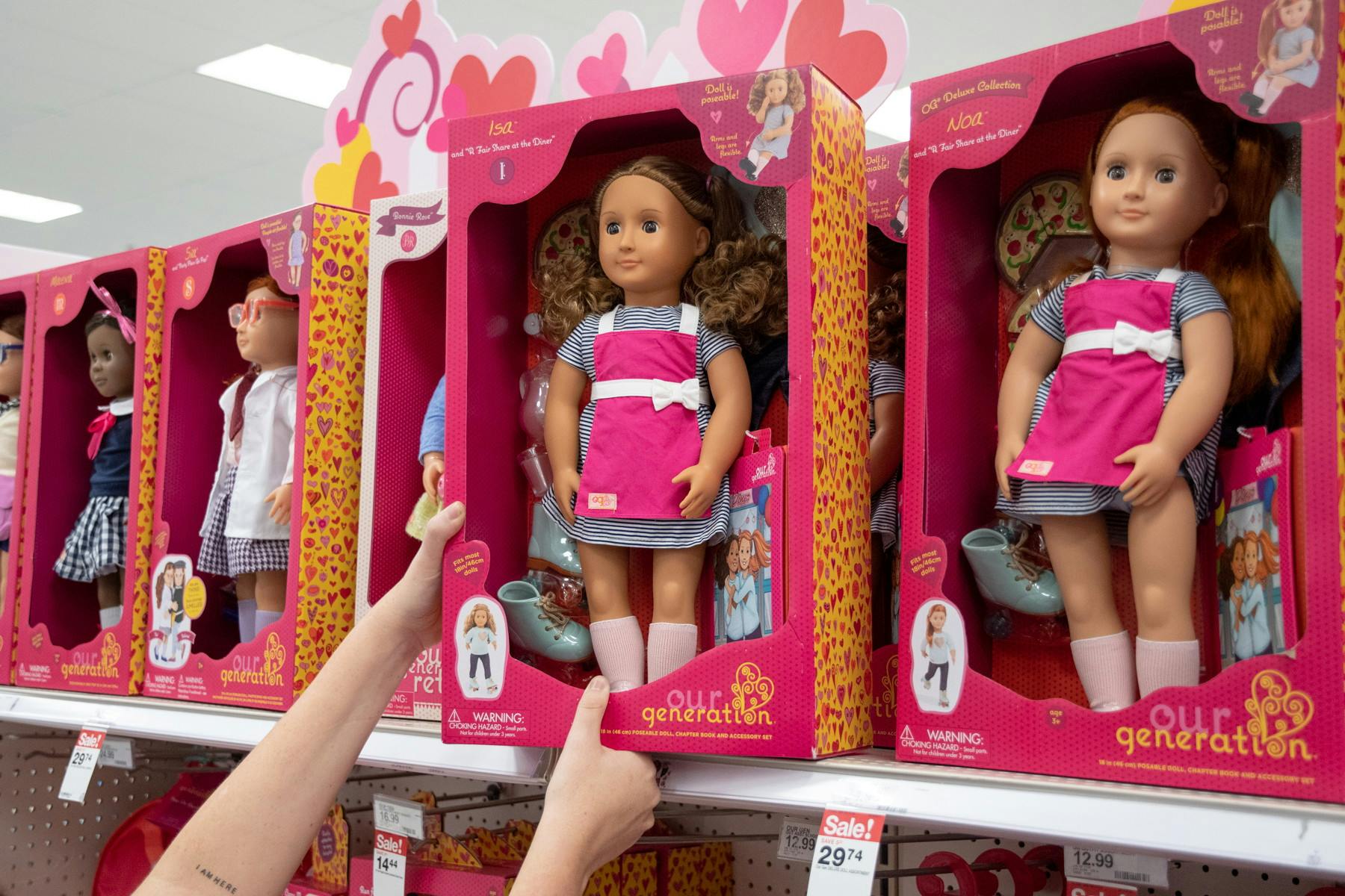 A person's arms reaching up to take an Our Generation doll off of the top shelf in the toy aisle at Target.
