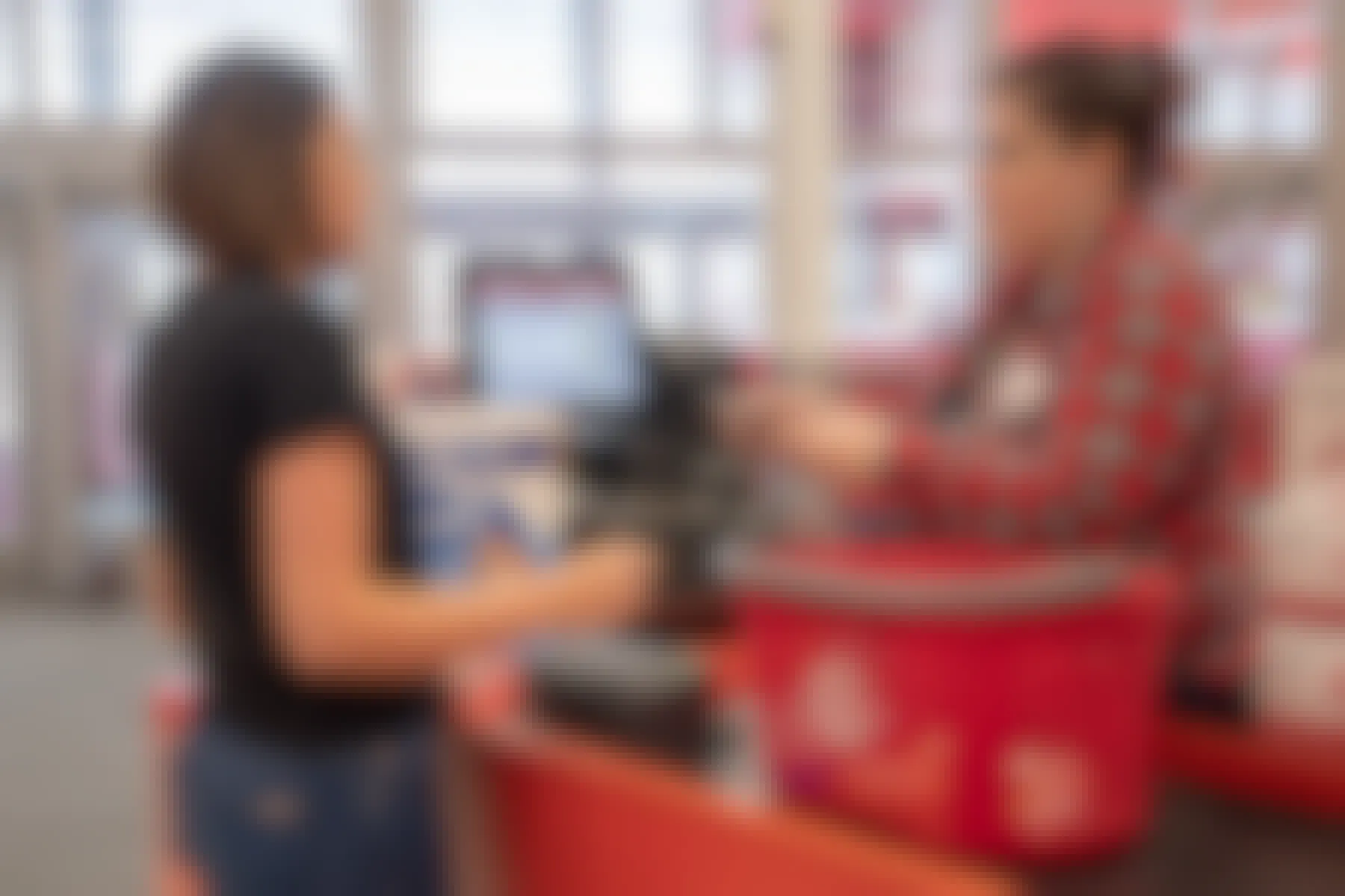 A woman standing at Target checkout with a basket on the conveyer belt and a cashier scanning her items.