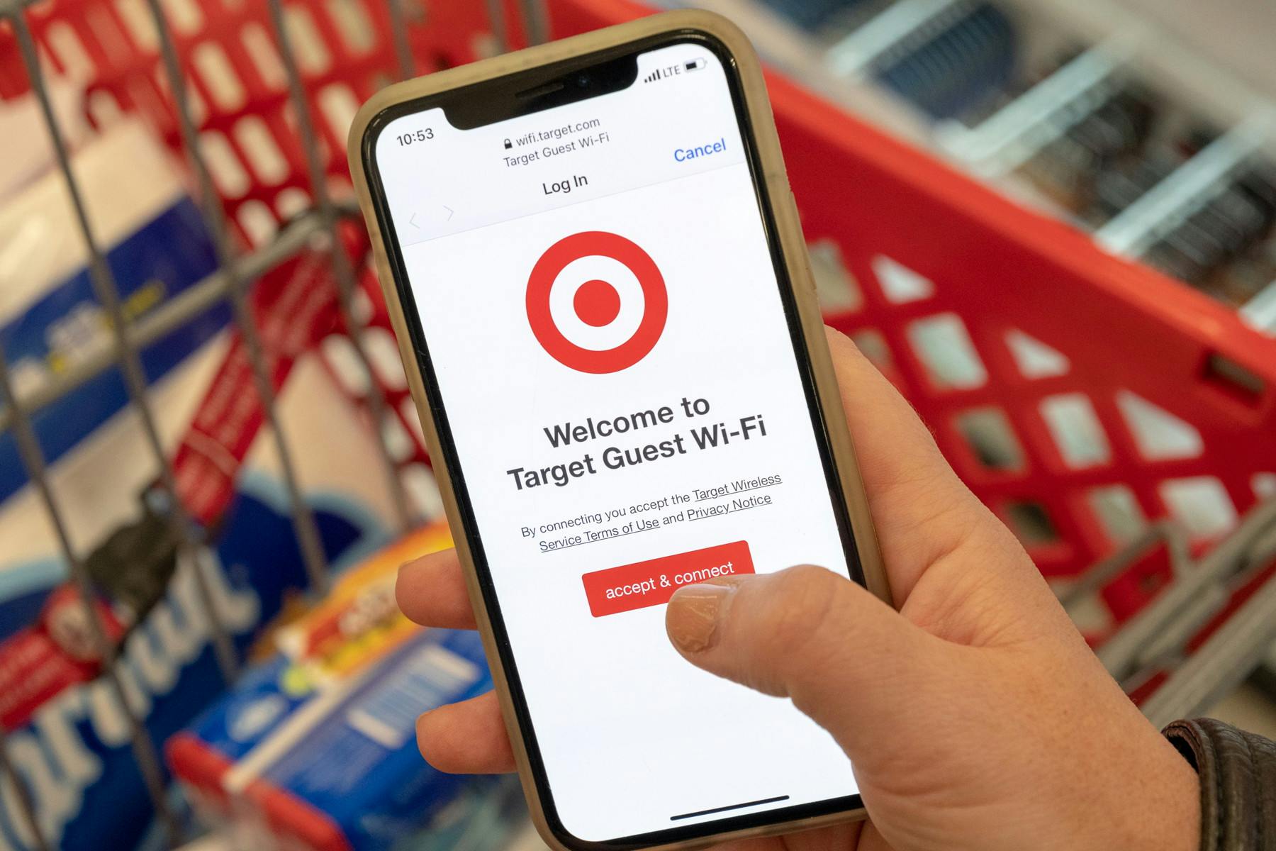 A person's hand holding a phone that is displaying the welcome screen for connecting to Target wifi above a Target shopping cart.