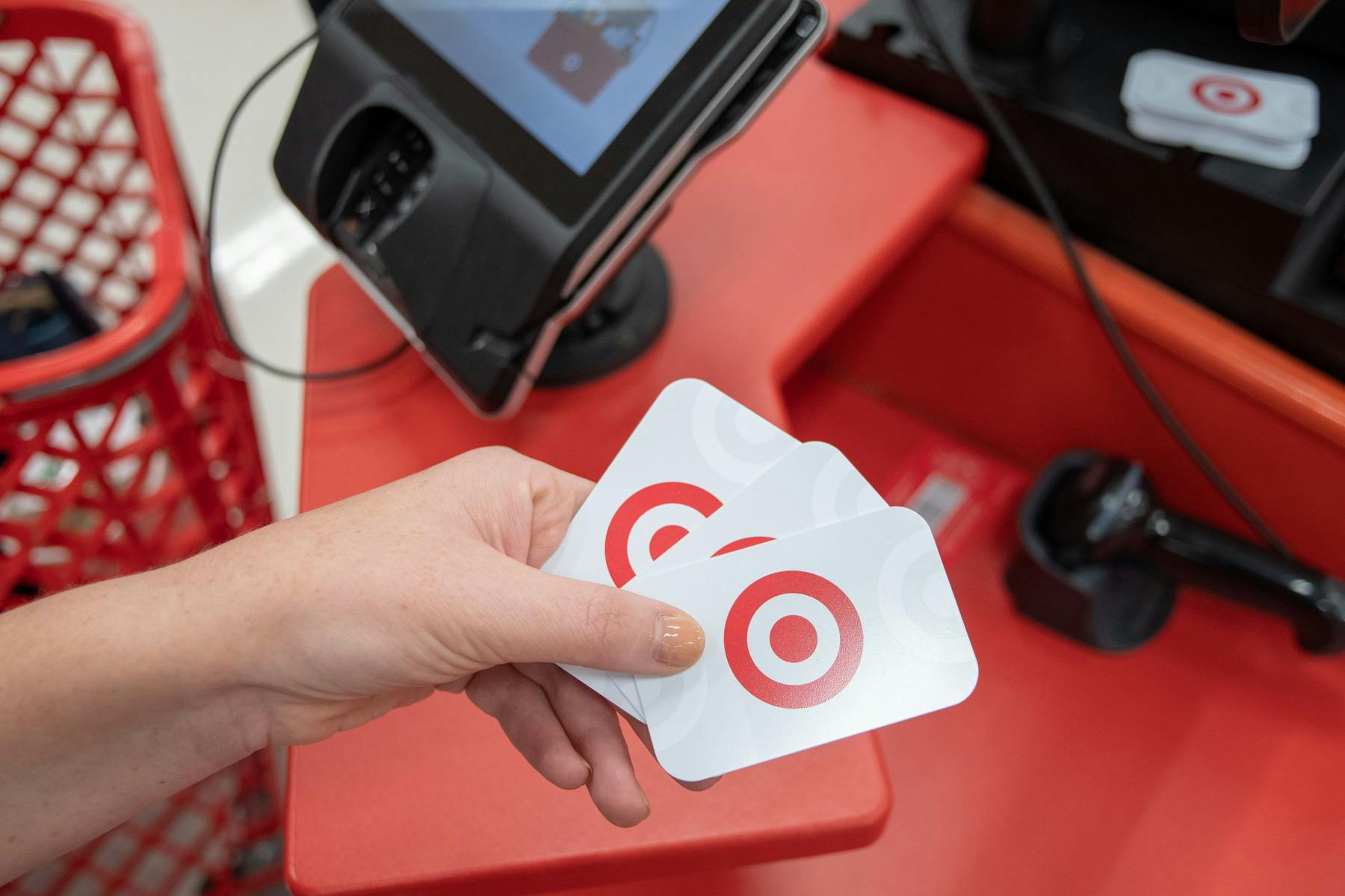 A person's hand holding three Target gift cards in front of the checkout counter at Target.