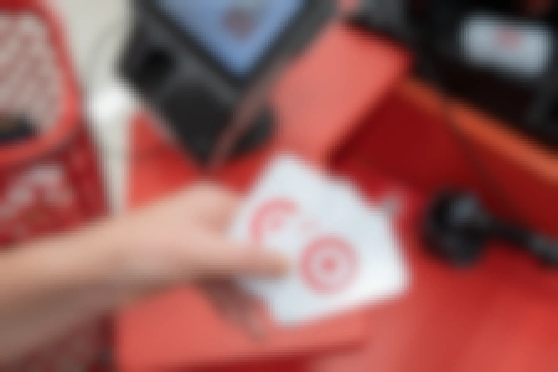 A person's hand holding three Target gift cards in front of the checkout counter at Target.