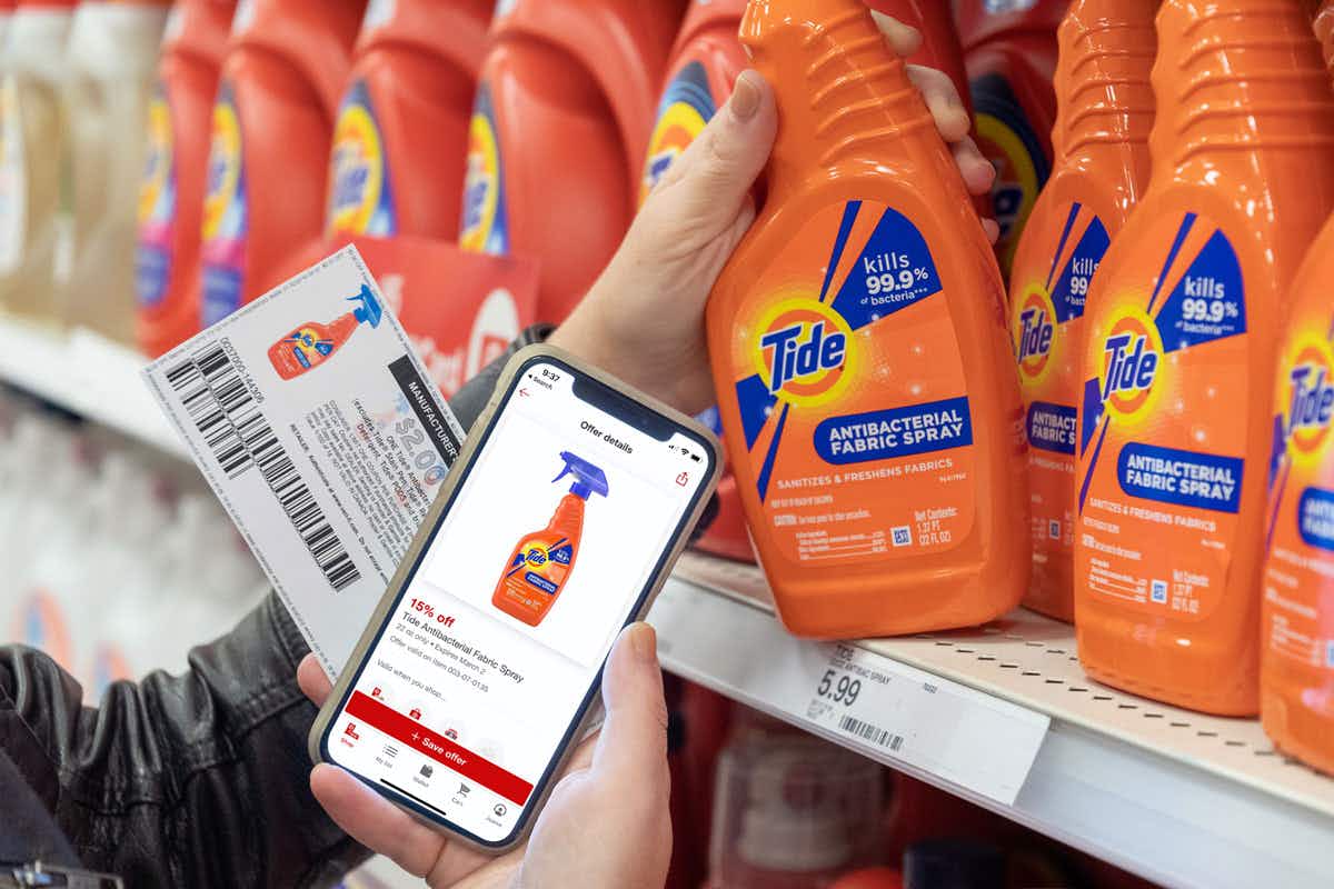 A person holding a manufacturer coupon and their phone displaying a TargetCircle offer next to a shelf full of Tide products.