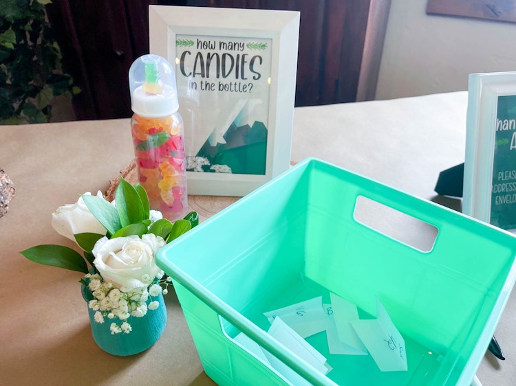 A baby bottle filled with gummy bears next to a sign that says how many candies in the bottle.