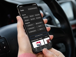 A person sitting in their car, using a phone displaying the Brickseek app.