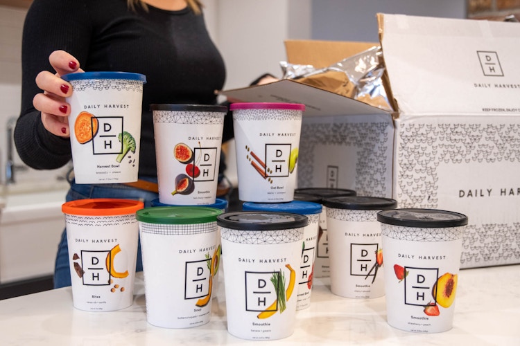 A woman pulling out the cups of food from a Daily Harvest meal kit box.
