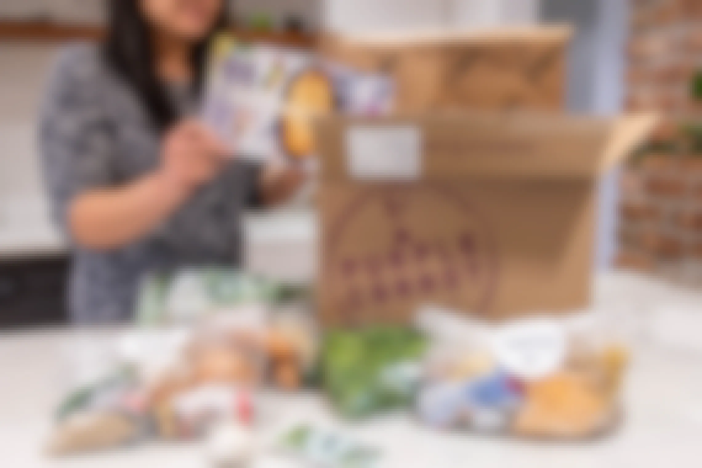 A woman unpacking the food from a Purple Carrot meal kit box.