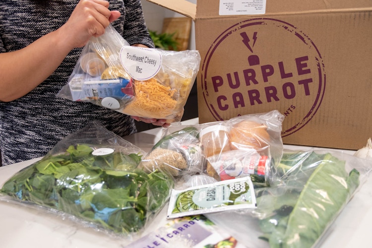 A woman unpacking the food from a Purple Carrot meal kit box.