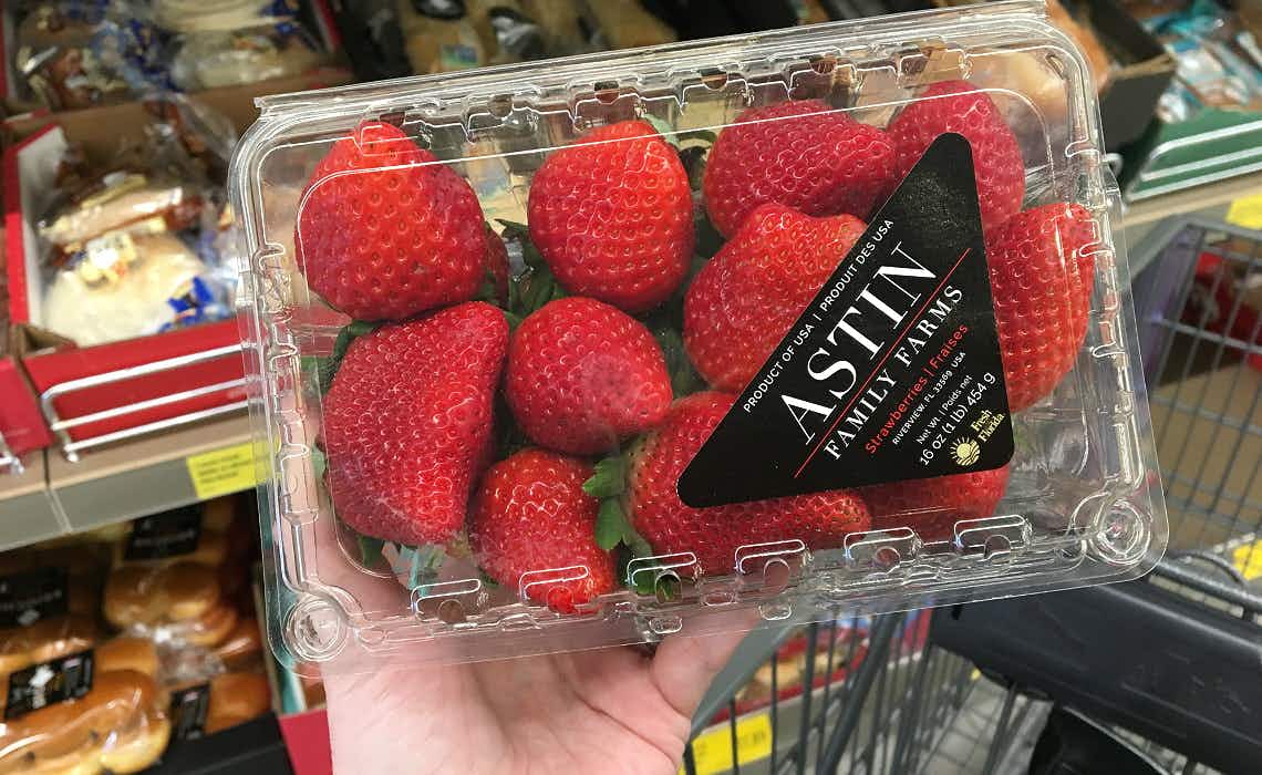 A person holding a container of strawberries in a grocery store.