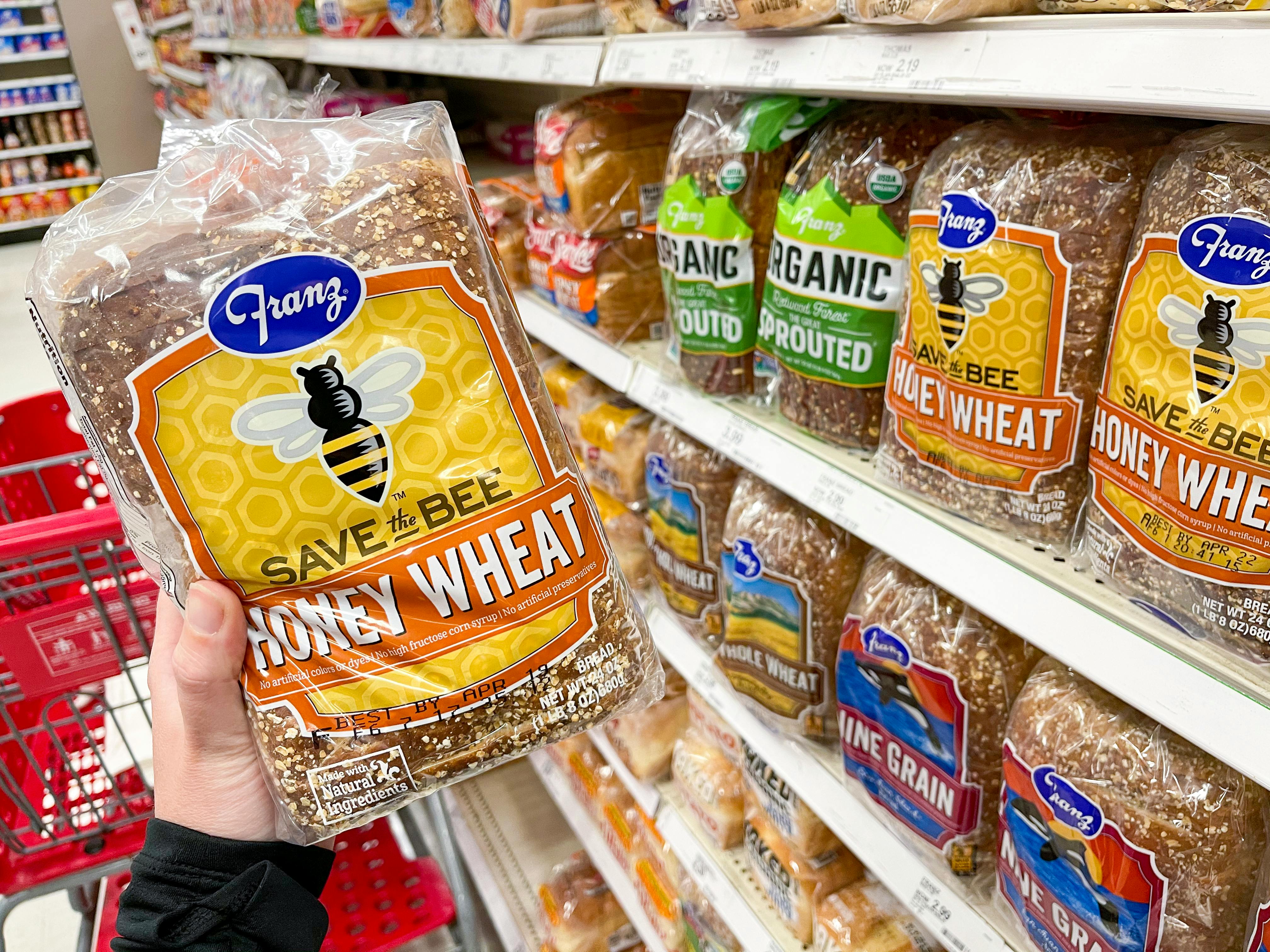 A person's hand holding a loaf of Franz Honey Wheat bread next to a shelf filled with bread at Target.