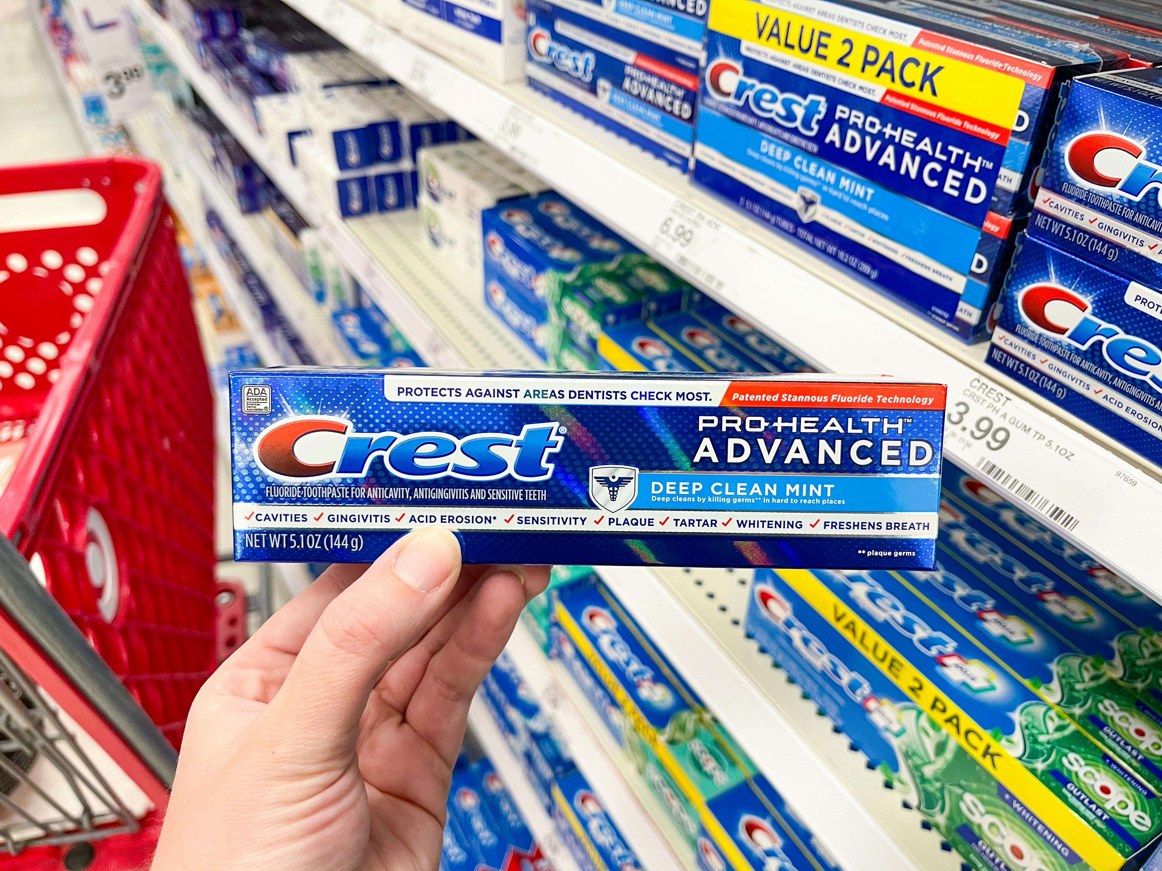 A person's hand holding a box of Crest toothpaste in the Target toothpaste aisle.