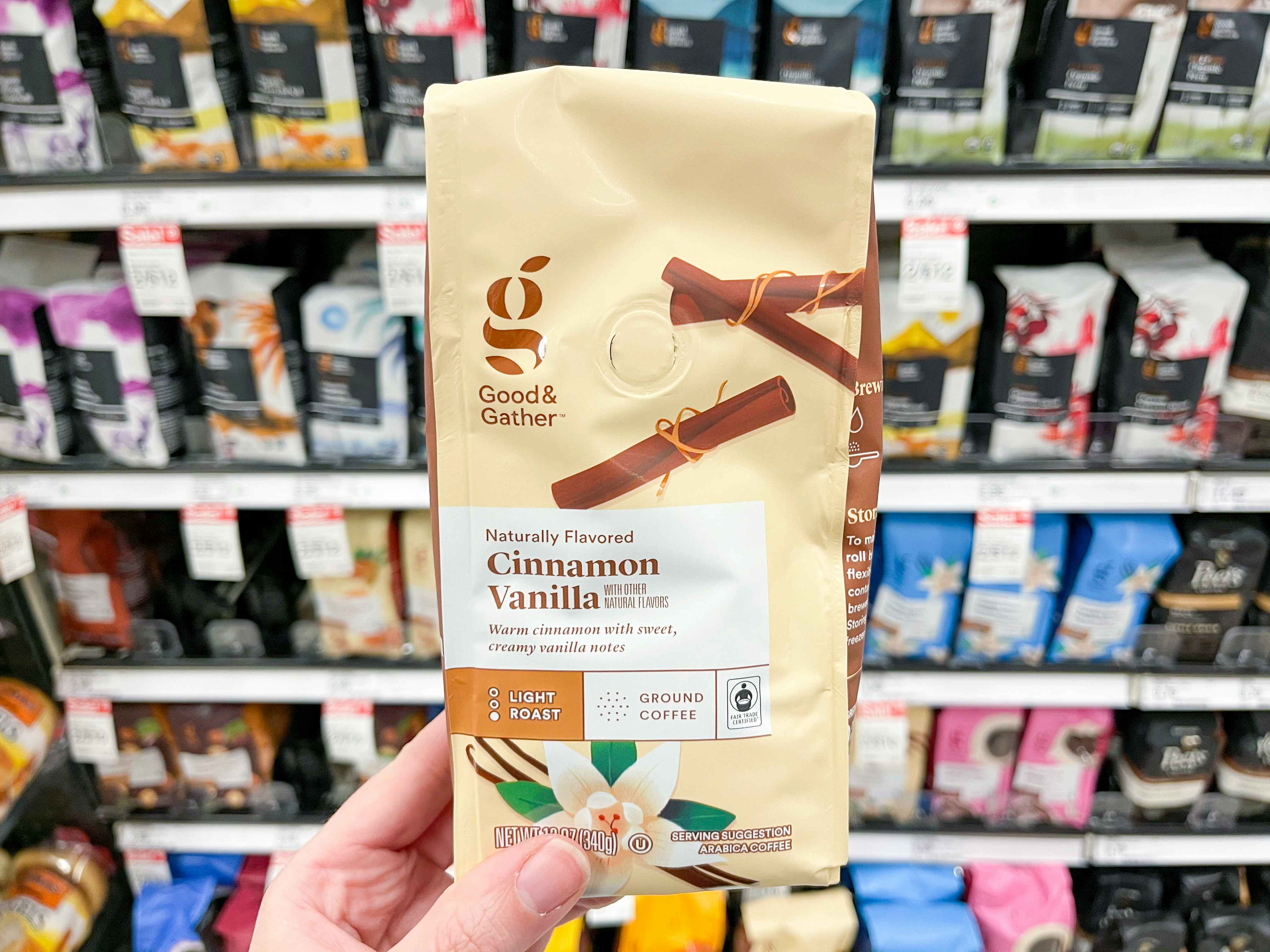 A person's hand holding a package of Good & Gather cinnamon vanilla coffee in the coffee aisle at Target.