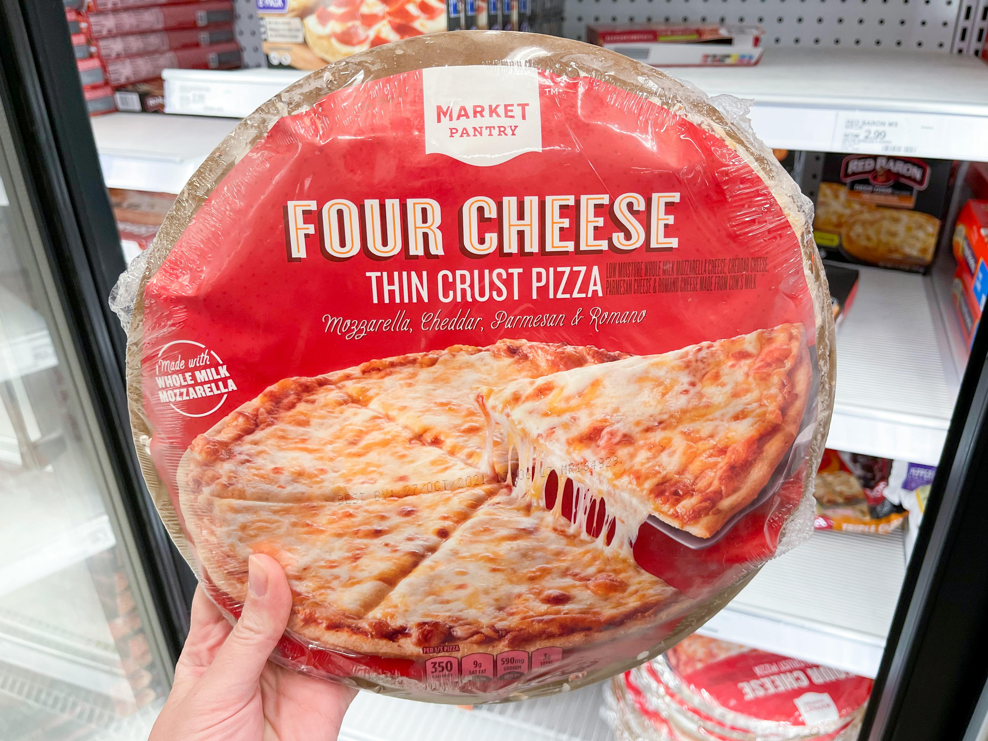 A person's hand holding up a four cheese Target brand pizza in the frozen food section.