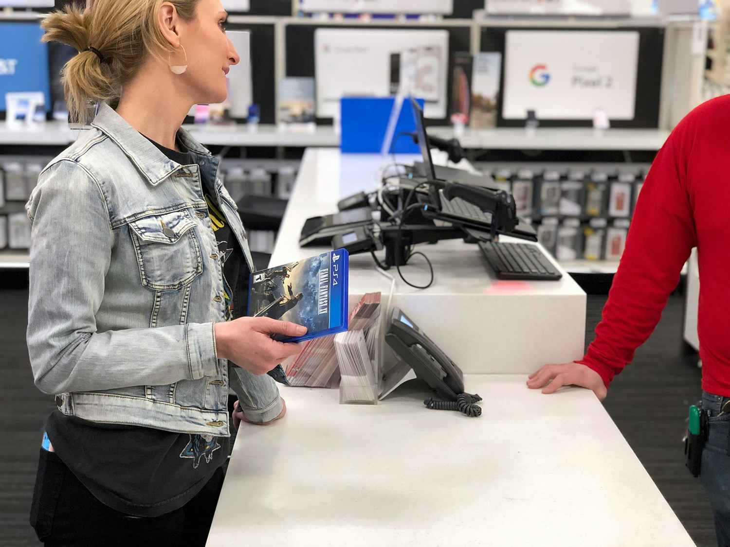 A woman standing at the counter in the electronics department at Target talking to an employee and holding a Call of Duty game.