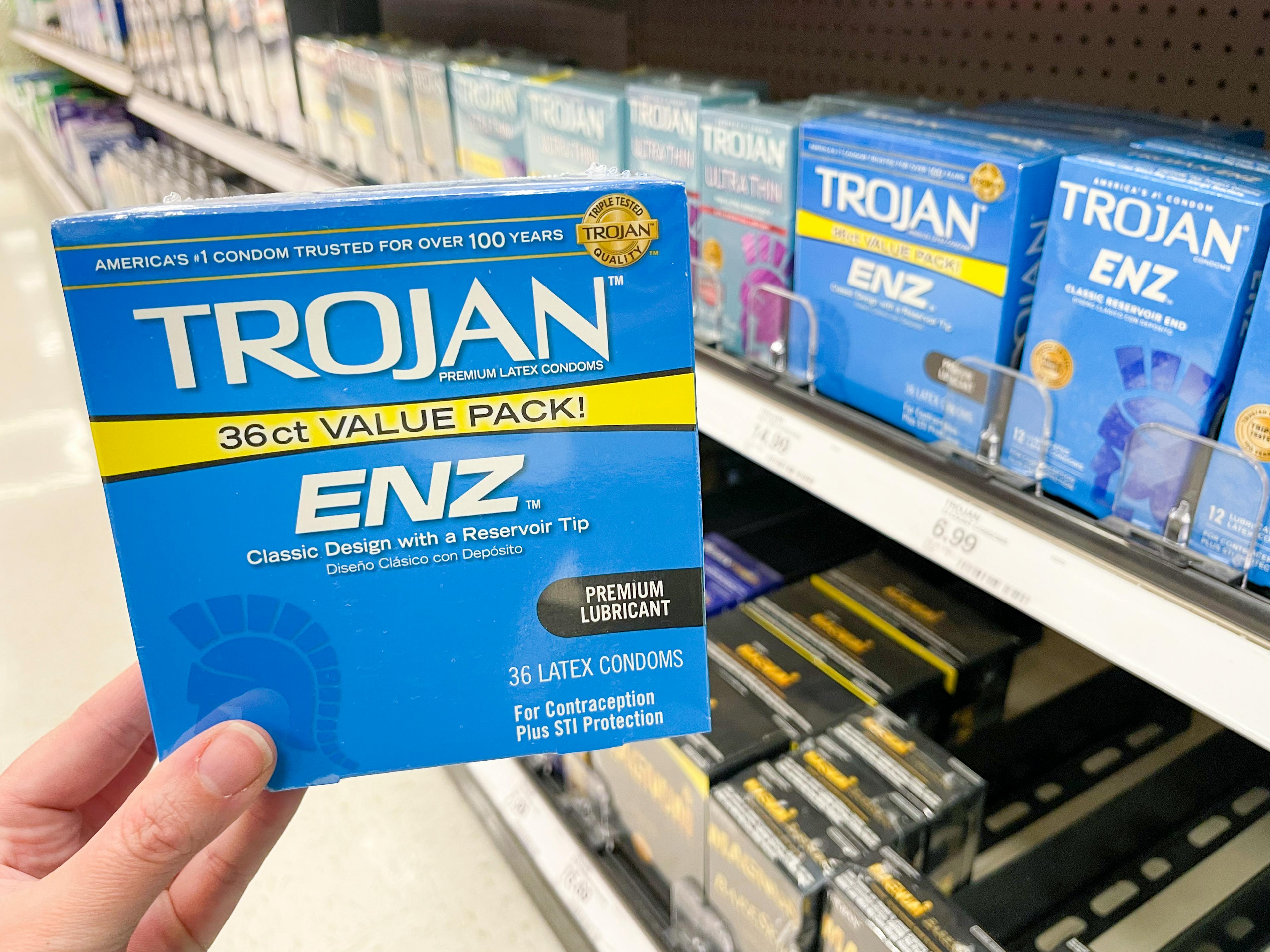 A person's hand holding a box of Trojan condoms in front of the condom shelf at Target.