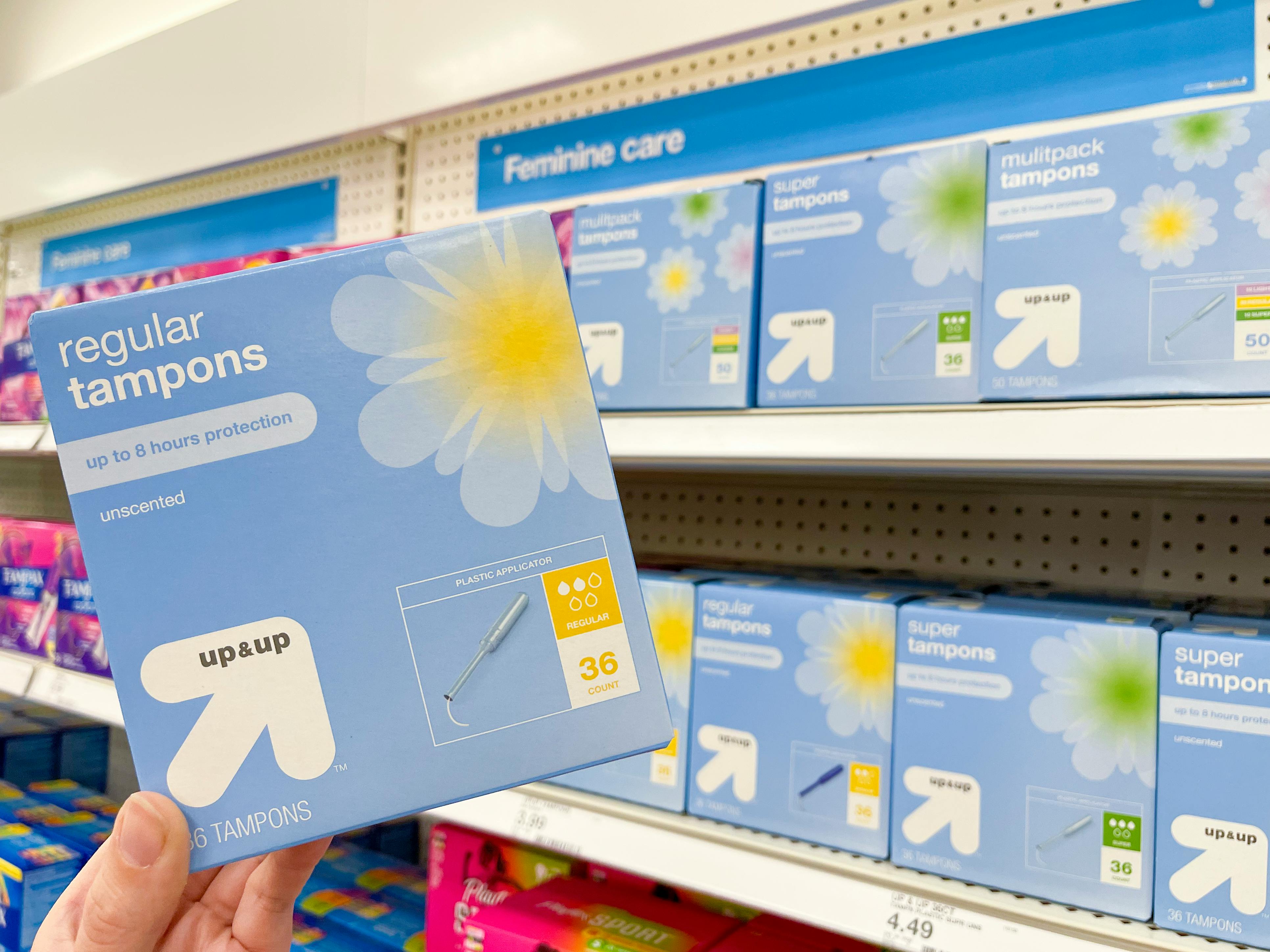 A box of Up&Up regular tampons being held next to a shelf of more of the same product inside Target