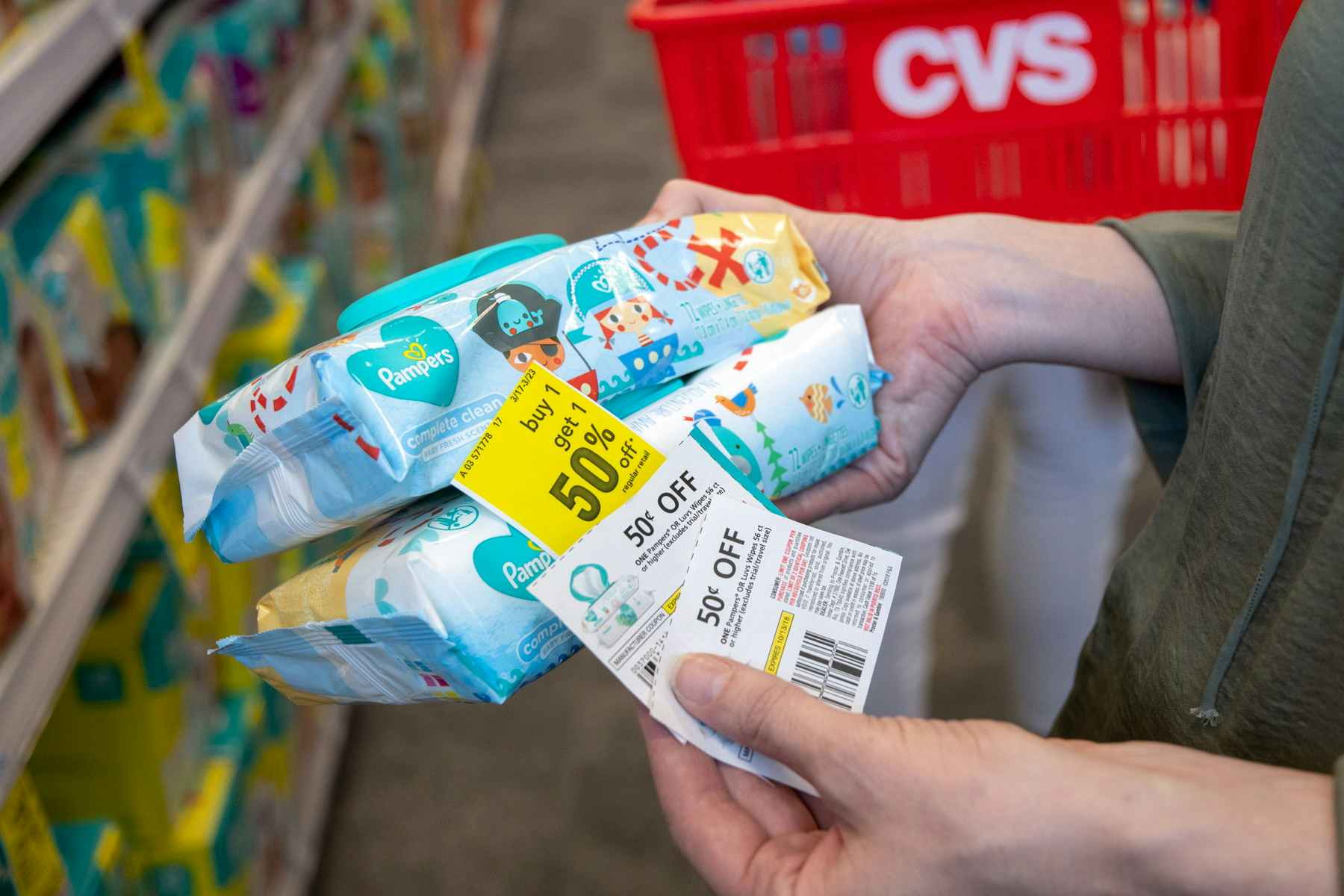 a person holding three coupons and two packages of baby wipes in front of a cvs cart.