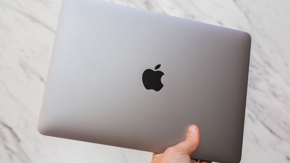 An apple macbook held in someones hand.