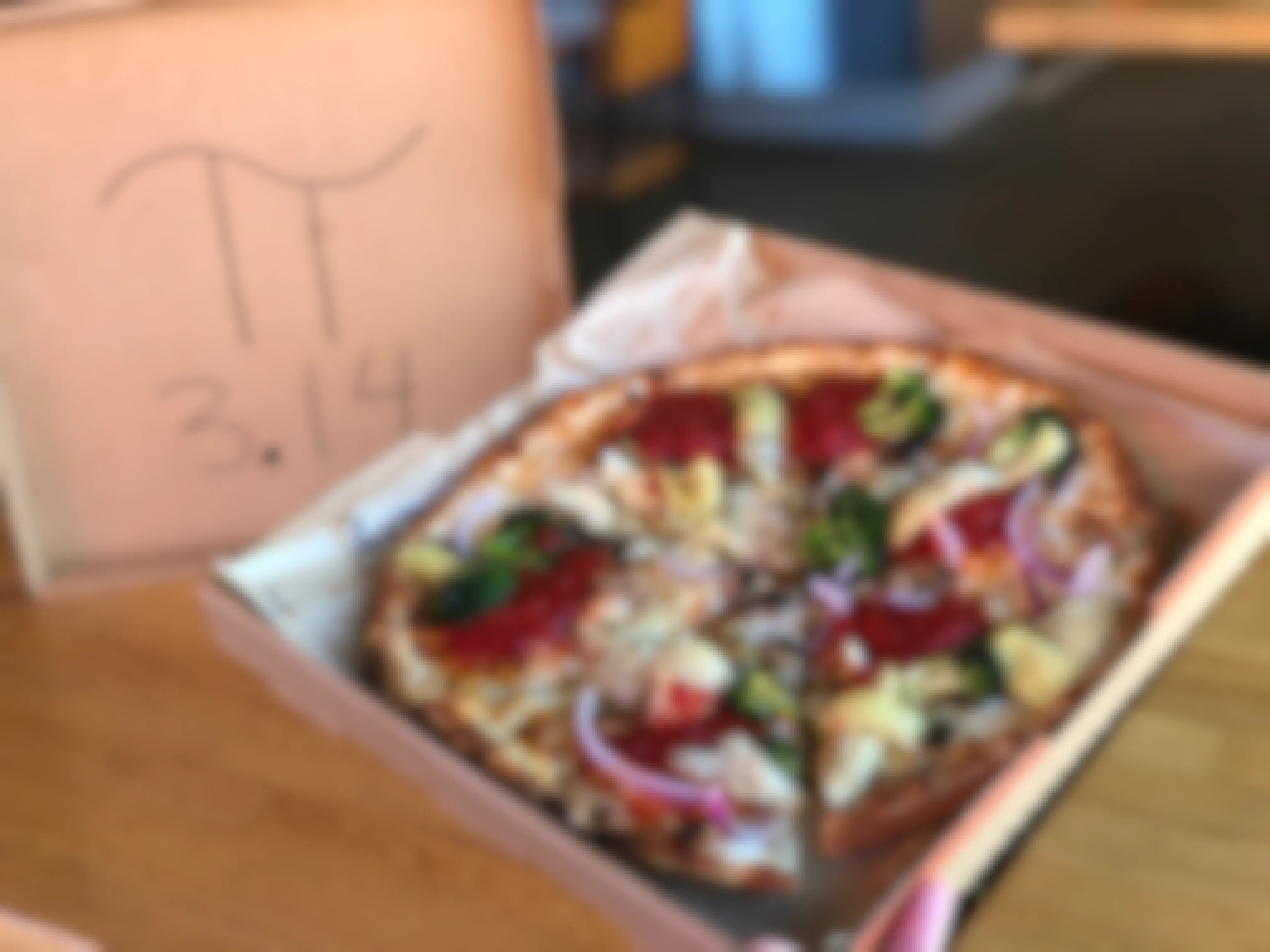 A Blaze pizza being held up inside of a box with no top. The top is displayed in the background with the Pi symbol and 