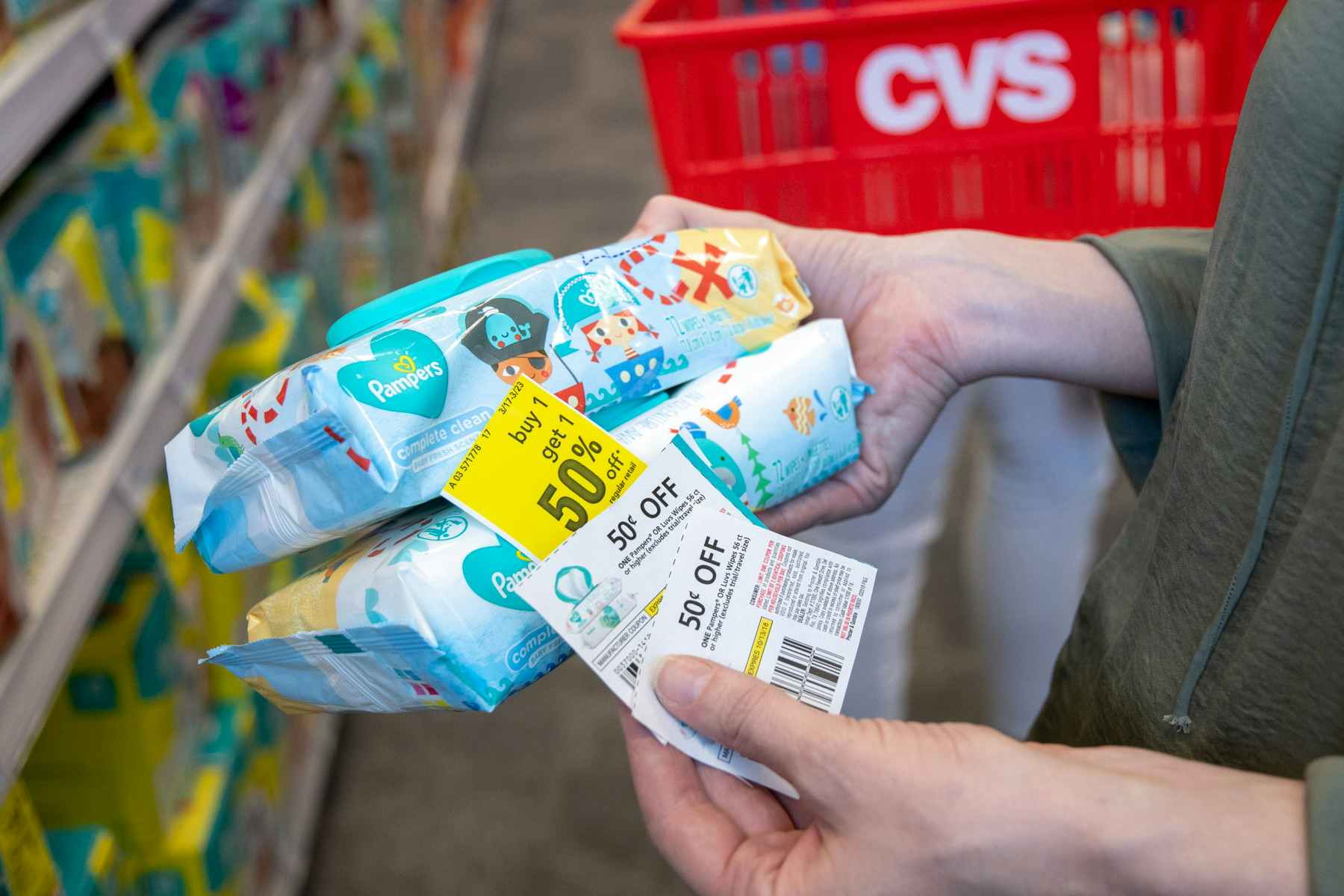 A woman holding two packs of pampers baby wipes with two coupons. A CVS basked it visible in the background.