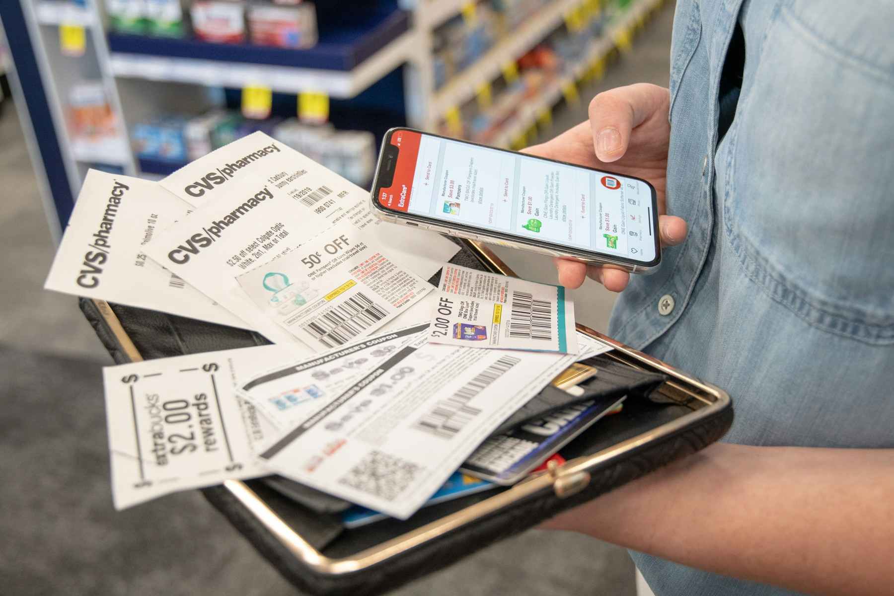 A person holding a cellphone with the CVS app displayed, while a stack of coupons sit in on a wallet in the person's other hand.