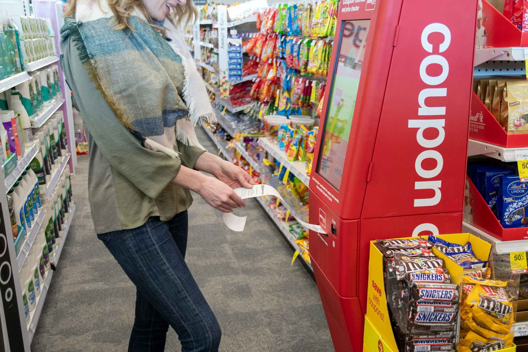 A woman holding a piece of paper with store coupons printed on it as the paper is dispensing out of a kiosk in CVS. 