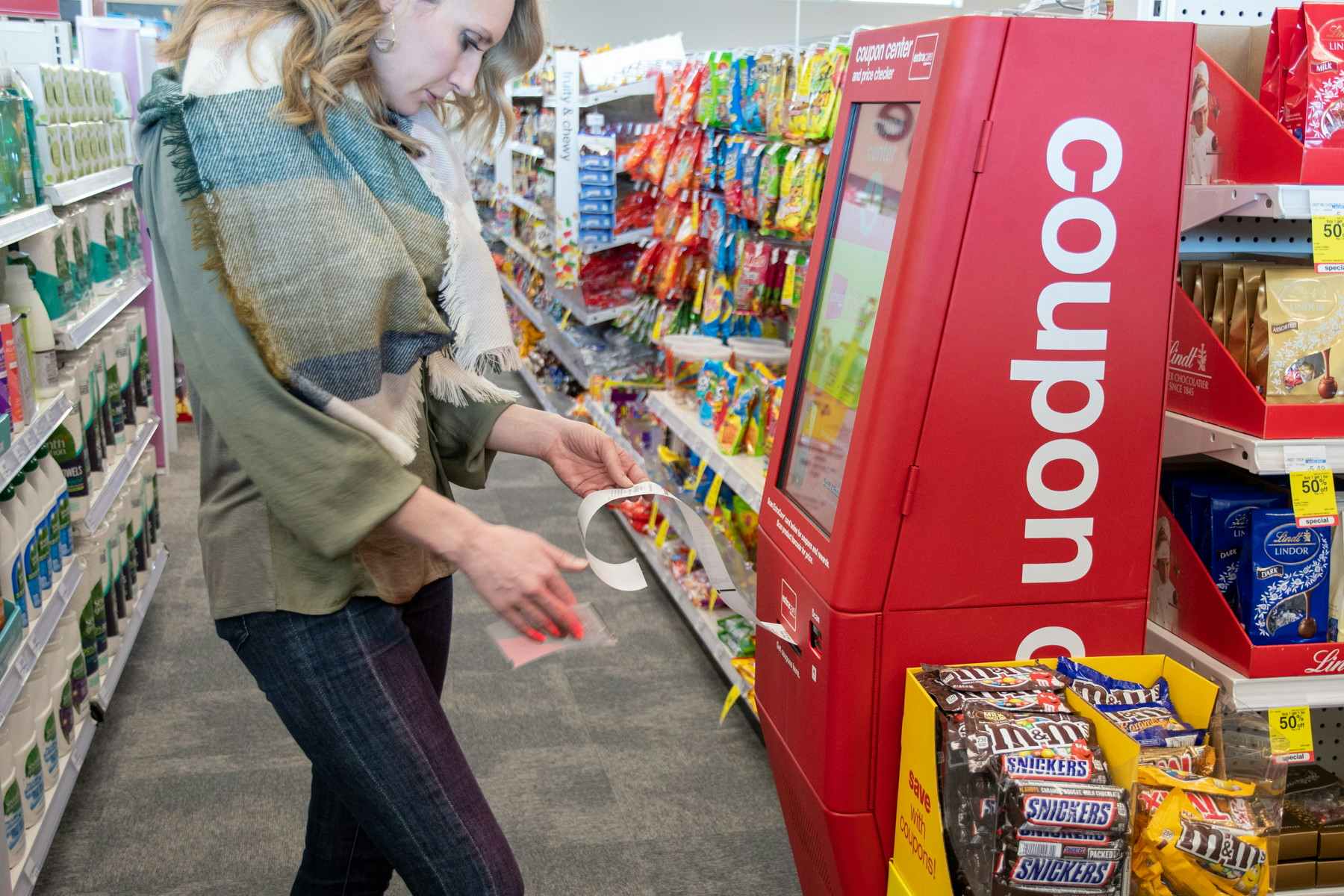 A woman standing and looking down at some coupons in front of a coupon machine at CVS.
