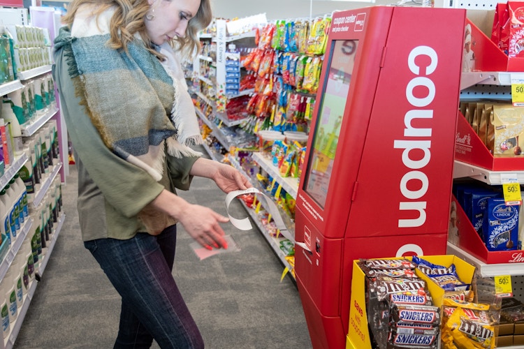 A woman standing and looking down at some coupons in front of a coupon machine at CVS.