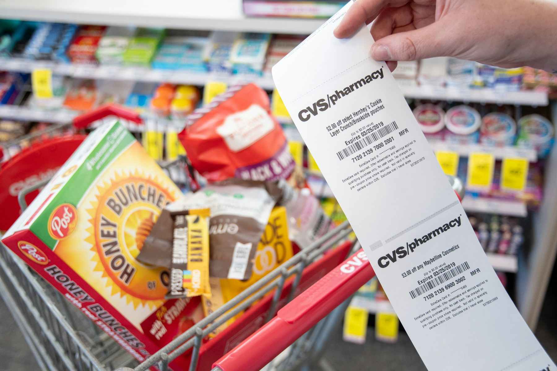 someone holding up cvs coupons in front of cart