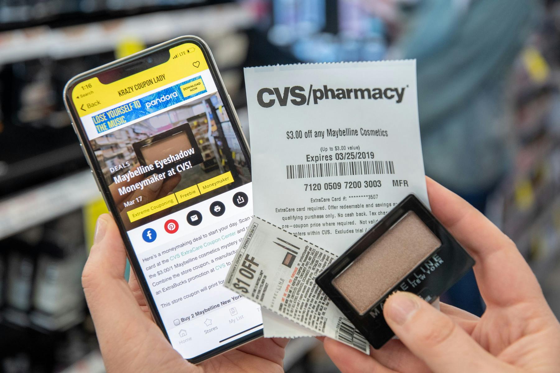 A person holding a smartphone in their left hand with the krazy coupon lady website displayed while holding eyeshadow along with coupons in the other hand.