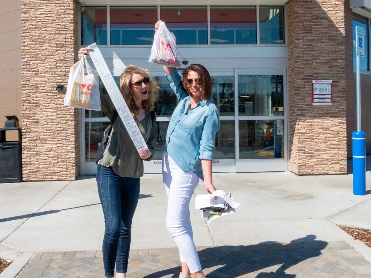 Two women posing outside of a CVS, showing the super long receipt