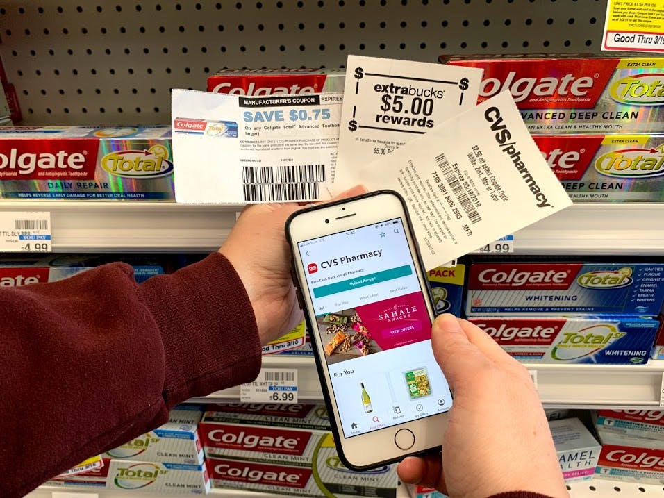 paper coupons for Colgate and CVS app being held in front of toothpaste