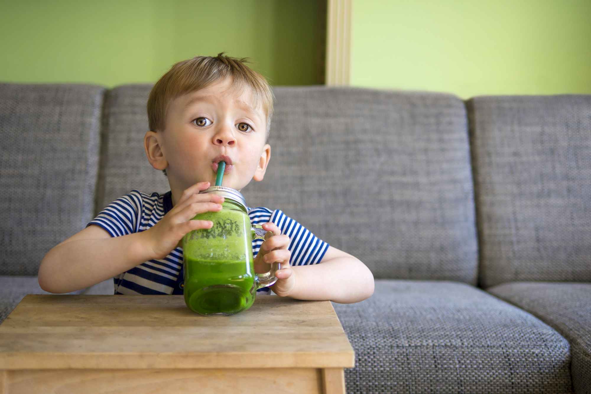 A child drinking a green smoothie out of a glass mug