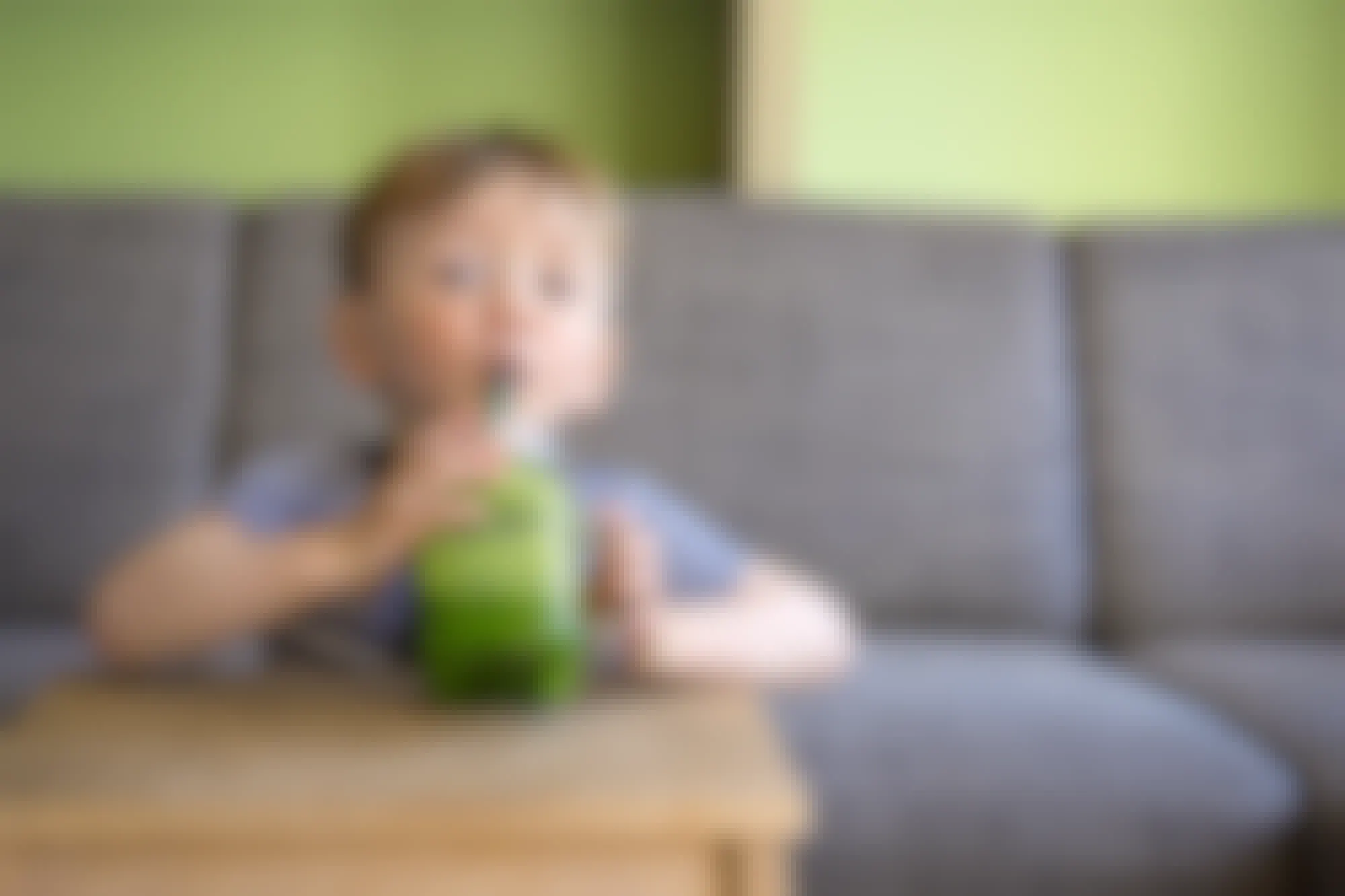 A child drinking a green smoothie out of a glass mug