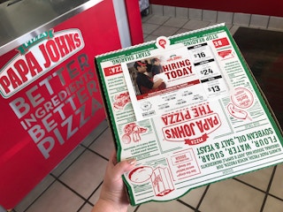 A person holding a Papa John's pizza near the counter at Papa John's.